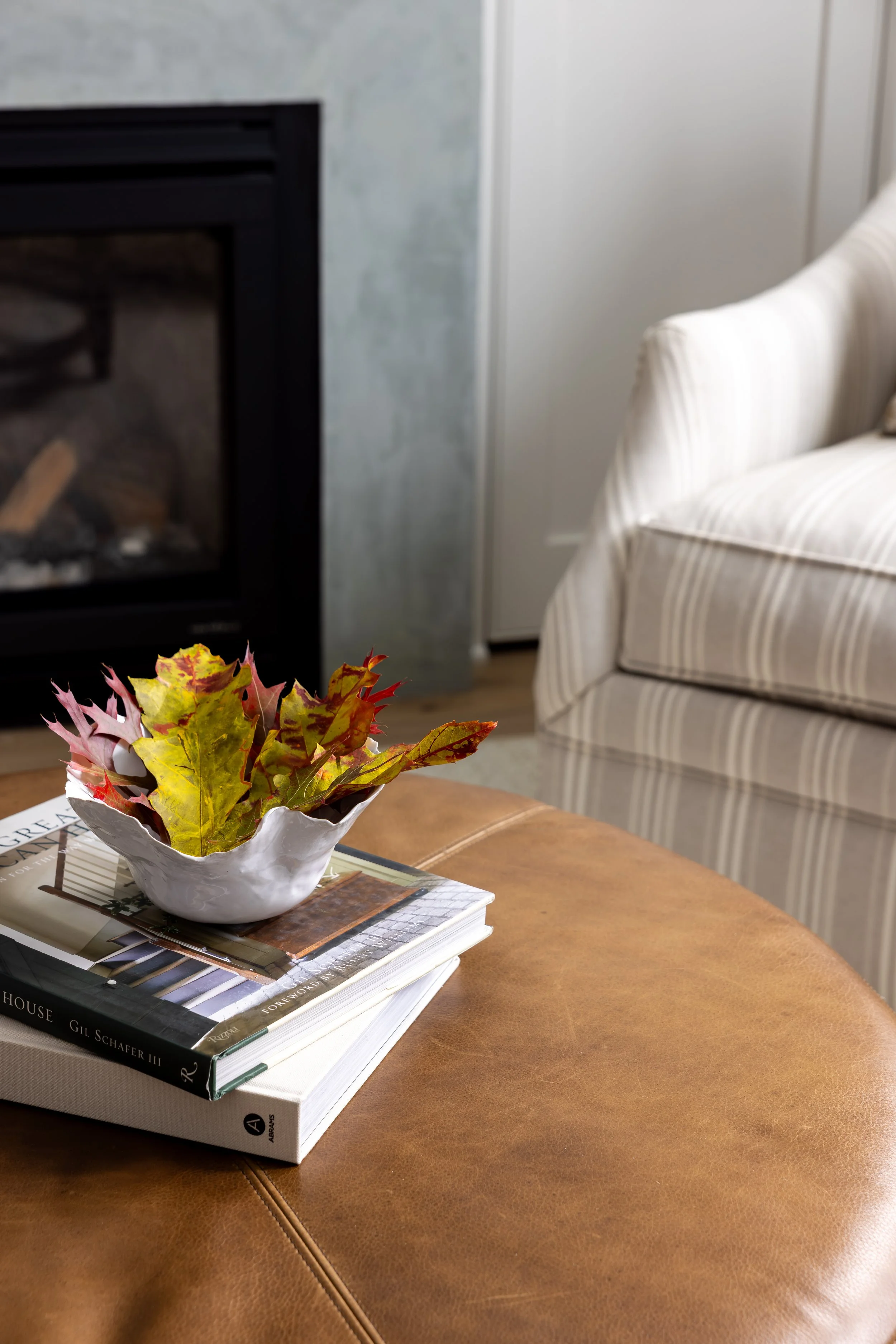 Leather ottoman detail with stacked coffee table books and ceramic floral arrangement beside fireplace — Bartlett Residence by Tama Bell Design, Ukiah CA
