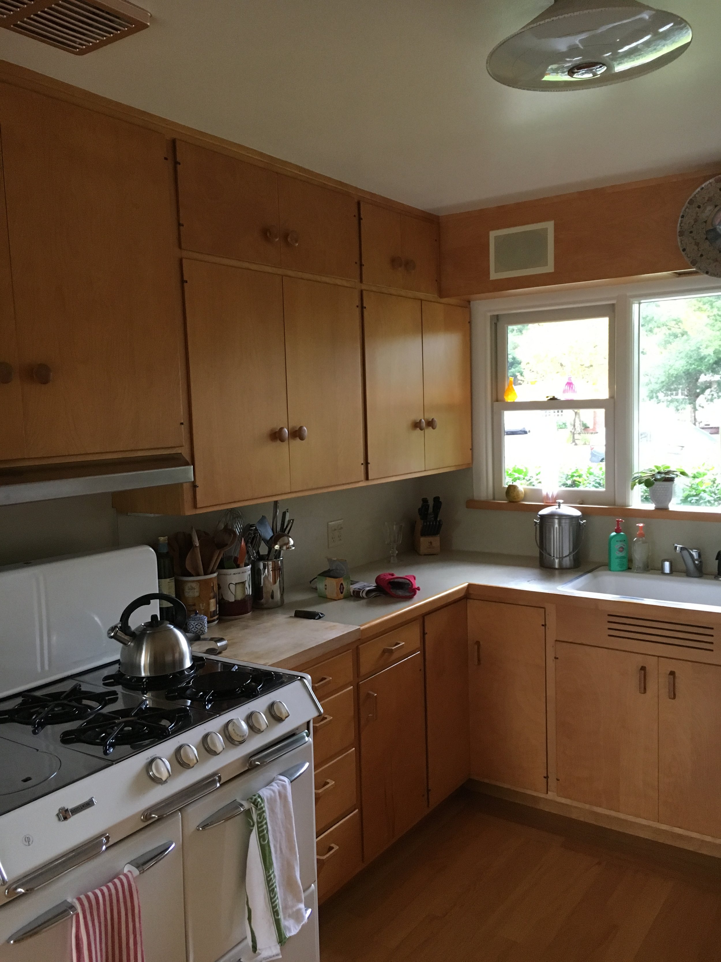  The same kitchen with warm wood cabinets from another angle. The window above the sink and dishwasher is visible. The white stove is protruding past the countertops.  