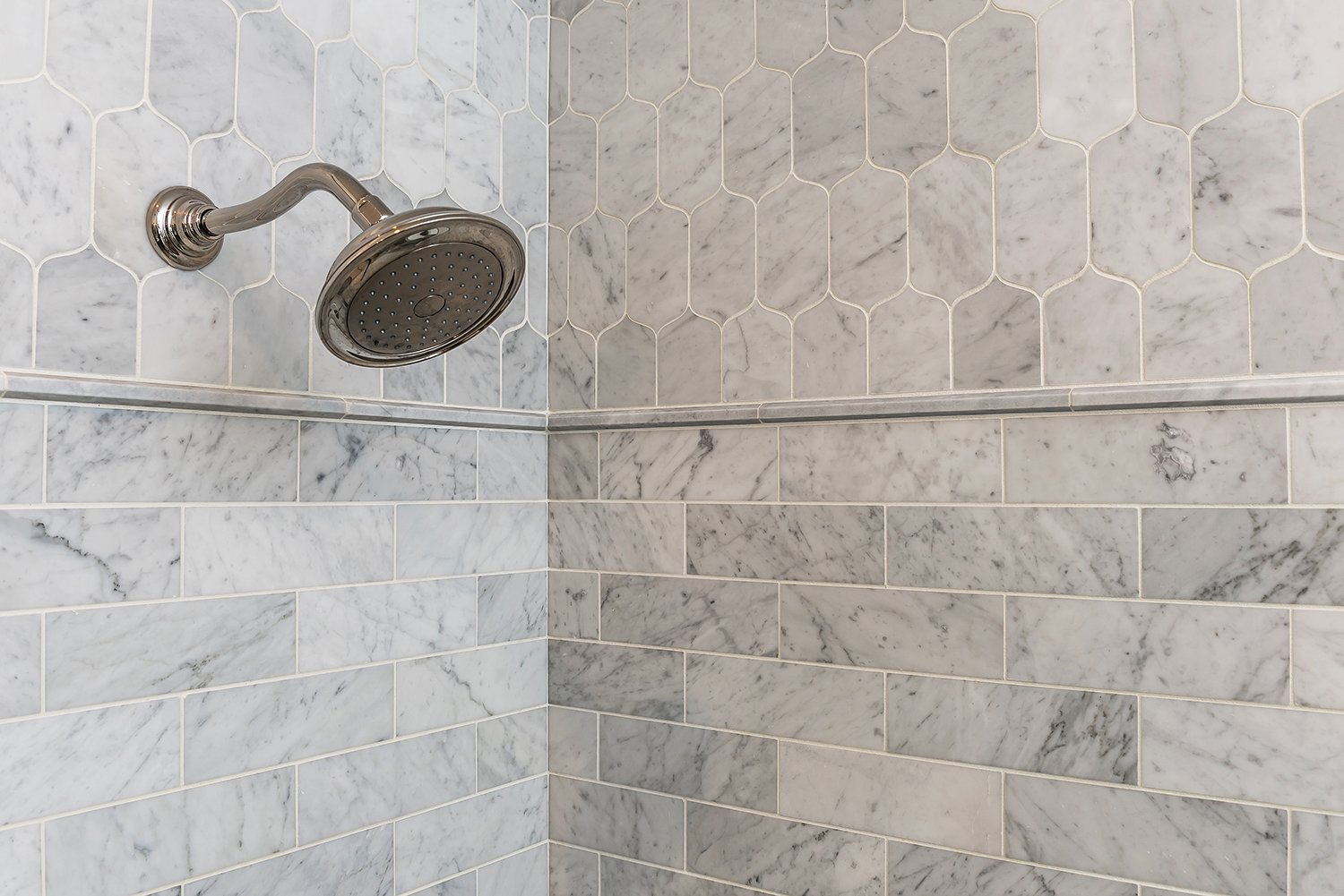  A close up of a tiled shower with a silver shower-head.  