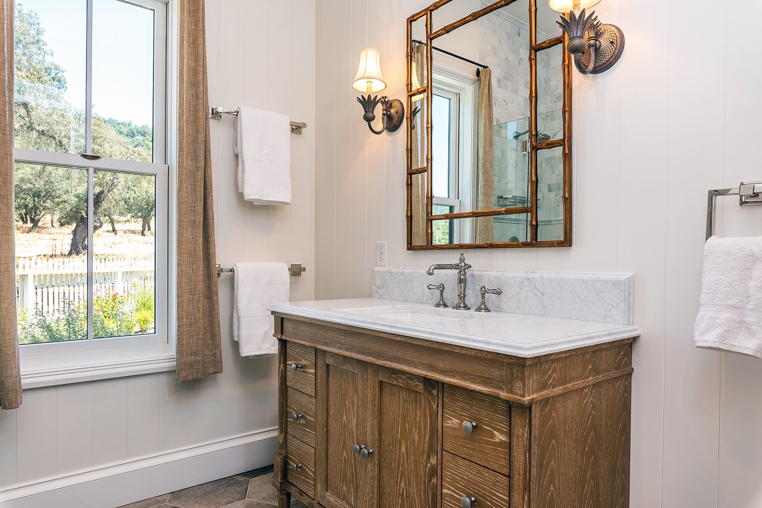  A bathroom with silver fixtures, an antique mirror, and wooden vanity.  