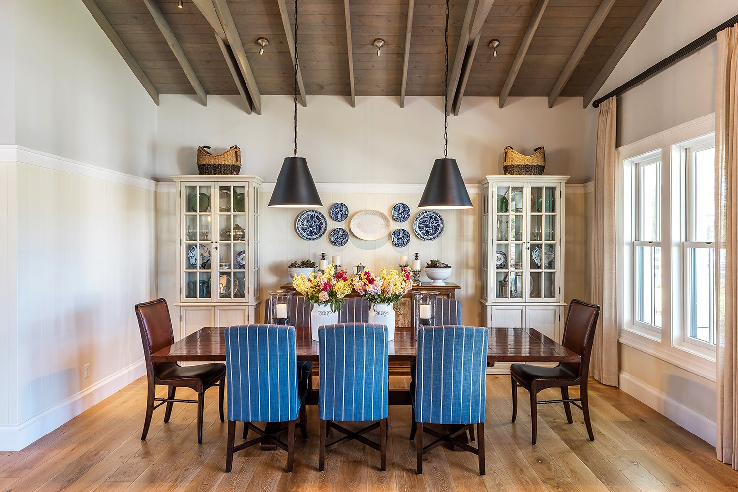  A dining area with black pendant lights, a dining table, and blue upholstered dining chairs.  