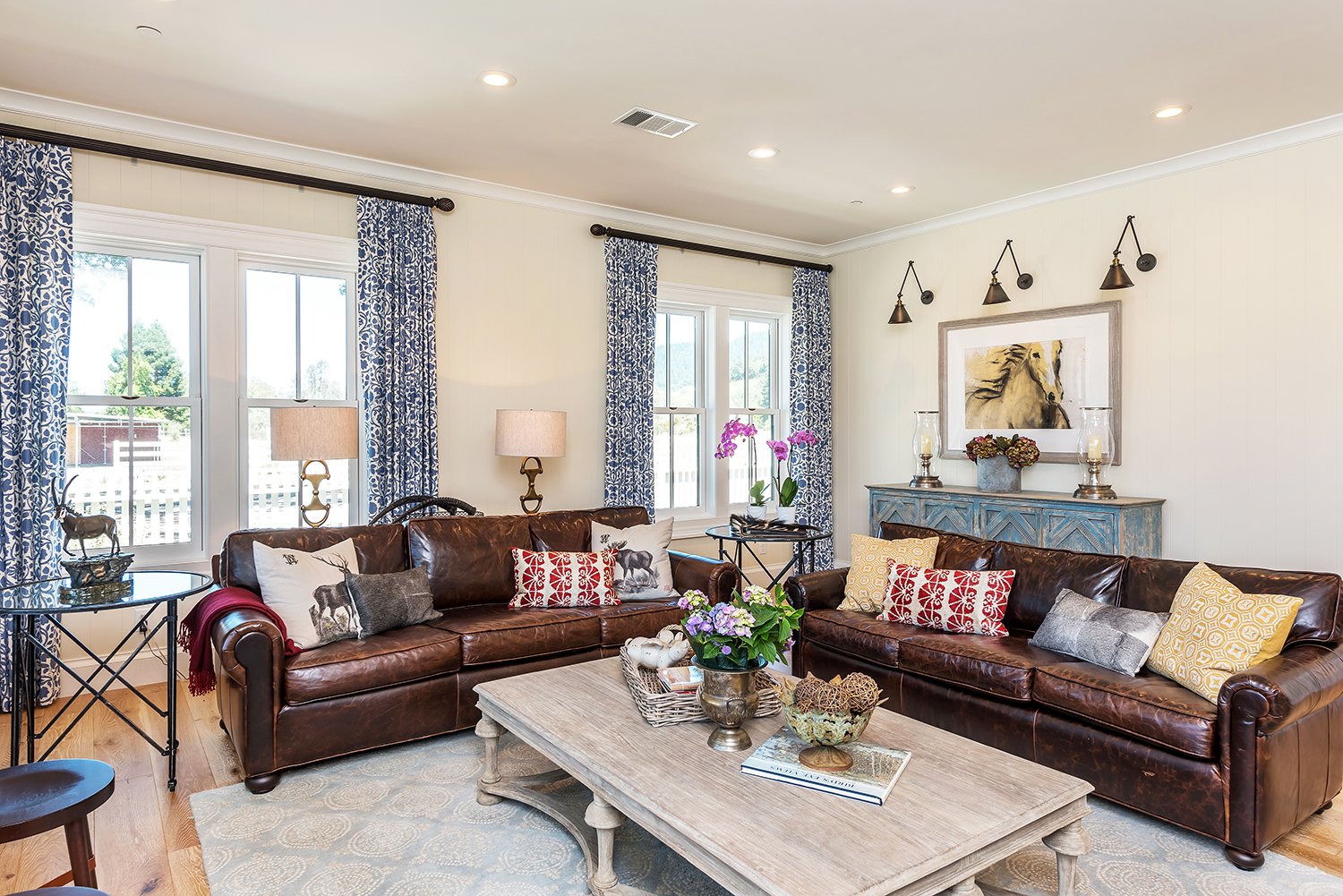  A living area with blue patterned curtains, a curated mantle, large coffee table, and two leather couches.  