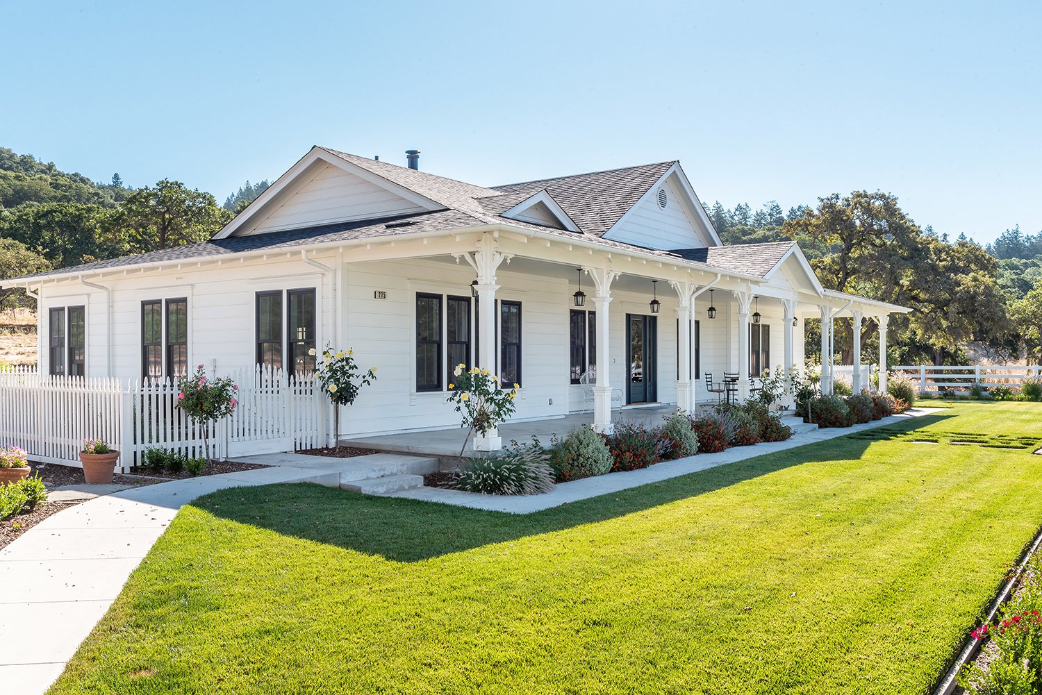  The exterior of a white home with a green lawn. A covered from porch with pendant lights is visible.  