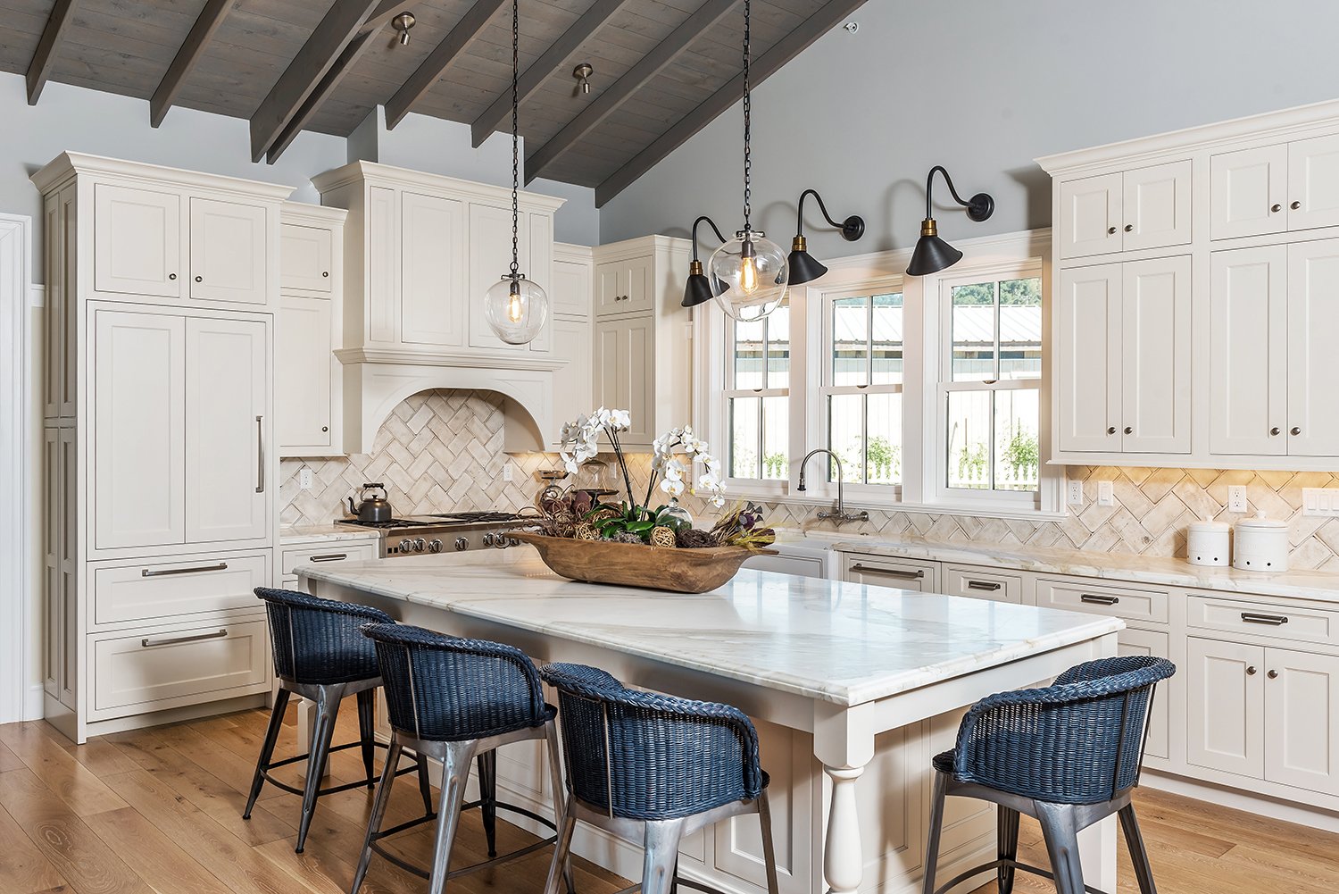  A kitchen island with blue wicker stools and glass hanging pendant lights.  