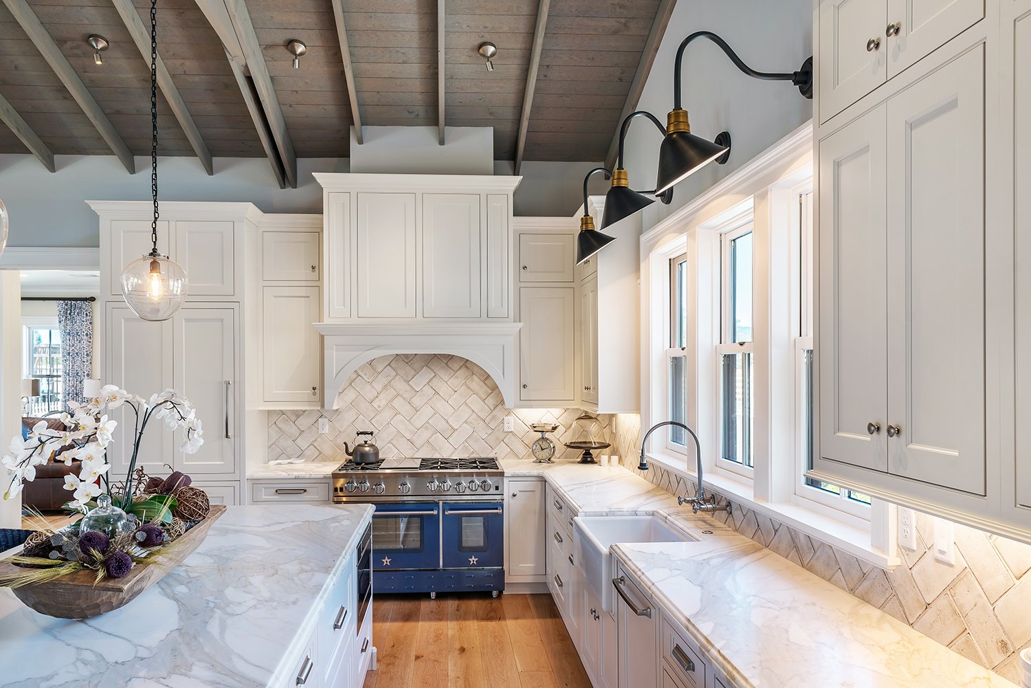  A kitchen with off-white angled tiled backsplash, wood flooring, white cabinets, and a statement blue range.  
