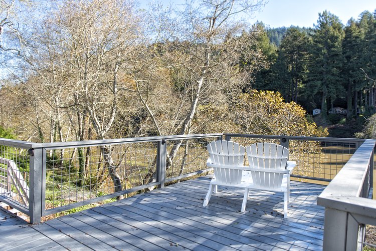  A wooden deck with paired Adirondack chairs. The deck overlooks trees.  