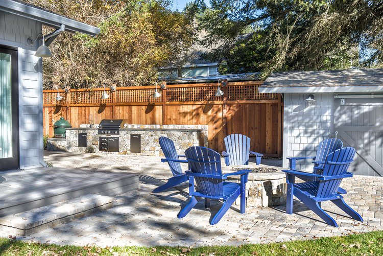  Four blue Adirondack chairs surrounding a raised outdoor fire pit.  