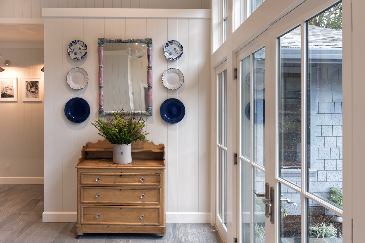  An antique style dresser with mirrors and plates hanging above it. A large floral arrangement sits on top of the dresser.  