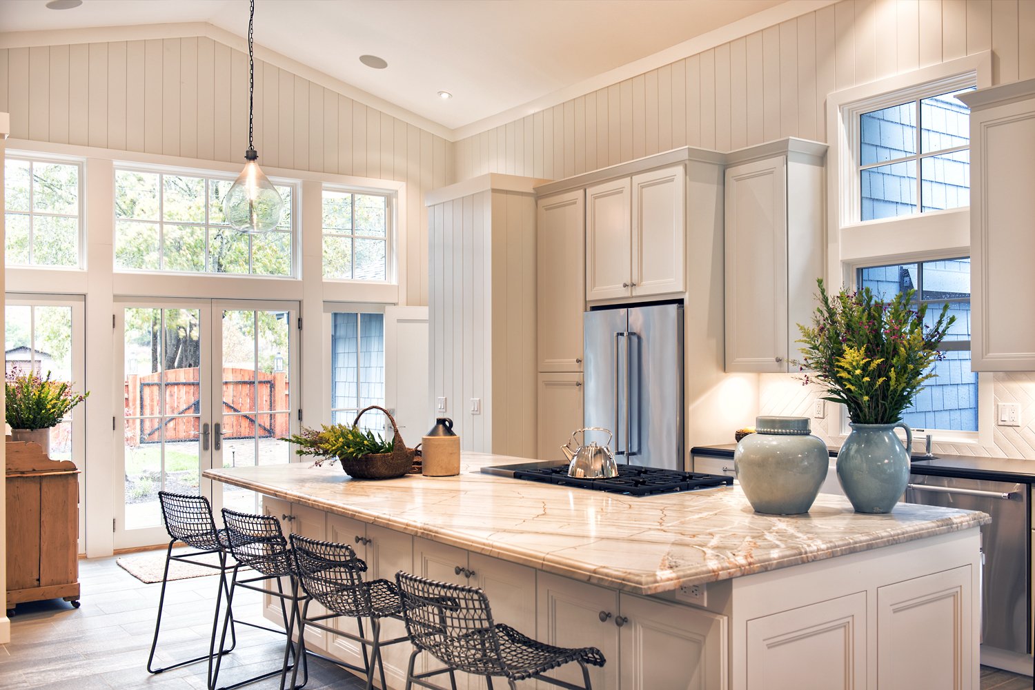  A large kitchen island with white cabinets and a refrigerator visible in the kitchen. The island has a built-in range.  