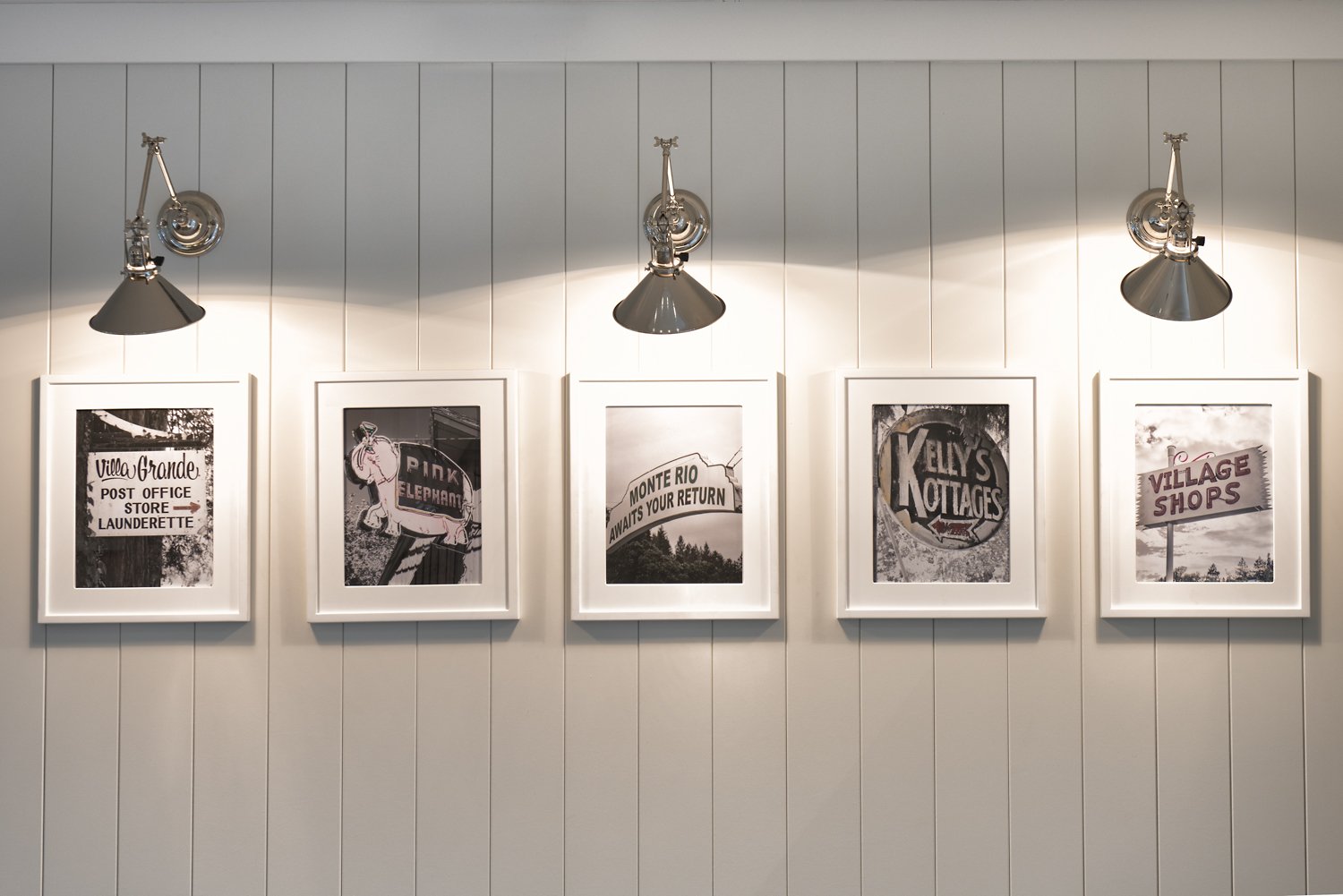  A gallery wall with black and white images of Monte Rio, lit with a silver sconce light.  