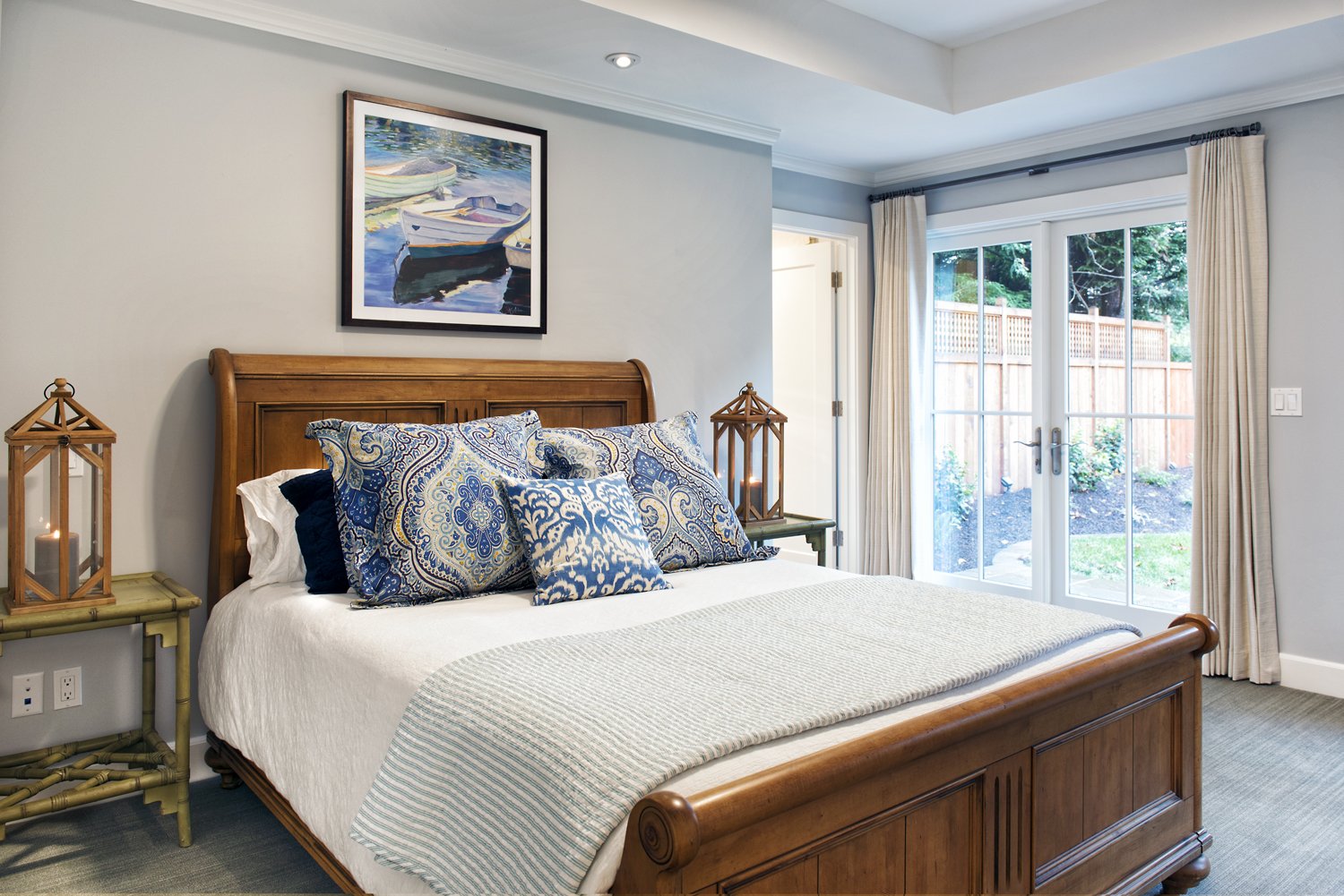  A bedroom with a wooden bed frame, painting of boats, and double doors to the yard.  