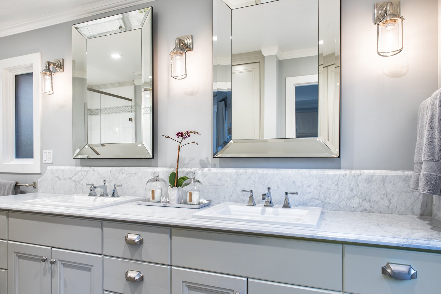  A bathroom with two sinks, large mirrors, and sconce lights.  