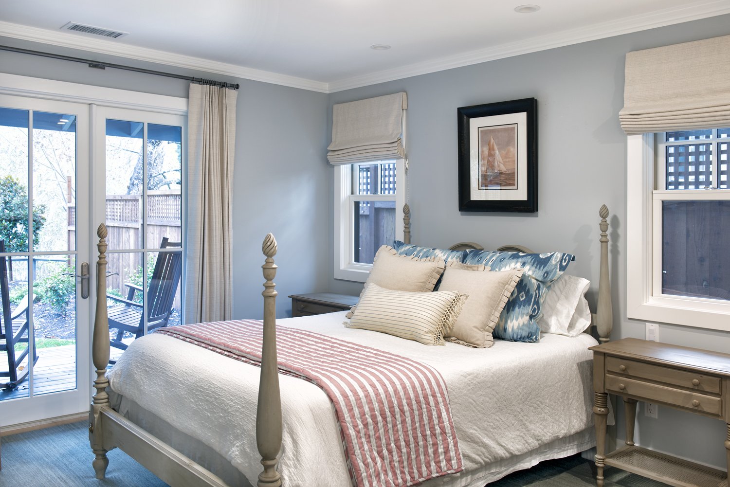  A bedroom with windows to the yard. The bed has vintage-style posts and patterned linens.  