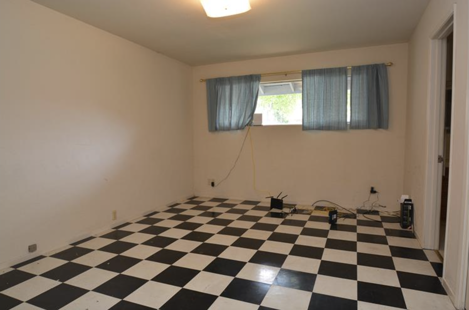  Before image of a room with windows on the upper half of the wall and a checkered linoleum floor.  