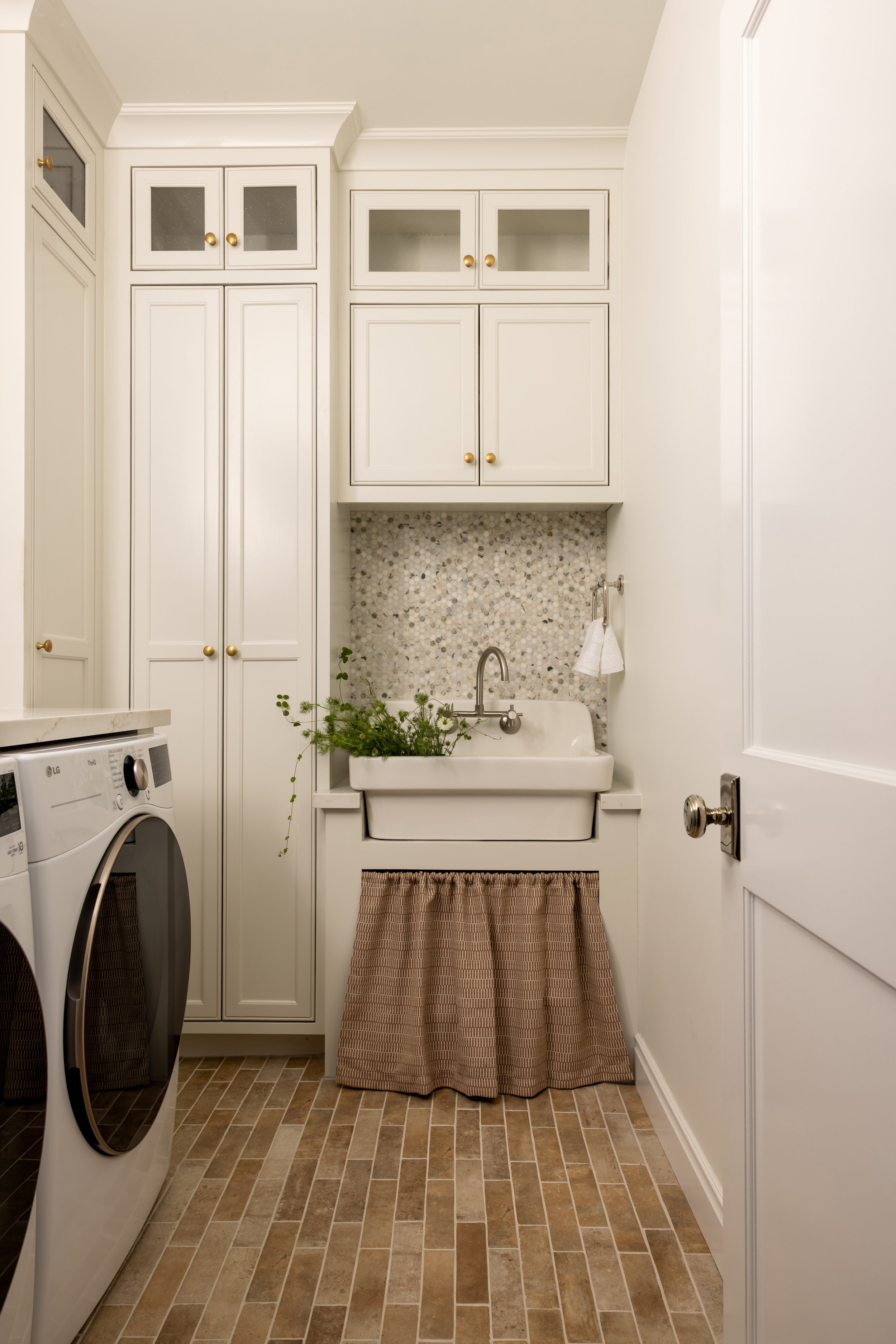 Transitional laundry room with farmhouse sink, mosaic tile backsplash, cream cabinetry, brass hardware, and linen curtain — Bartlett Residence by Tama Bell Design, Ukiah CA