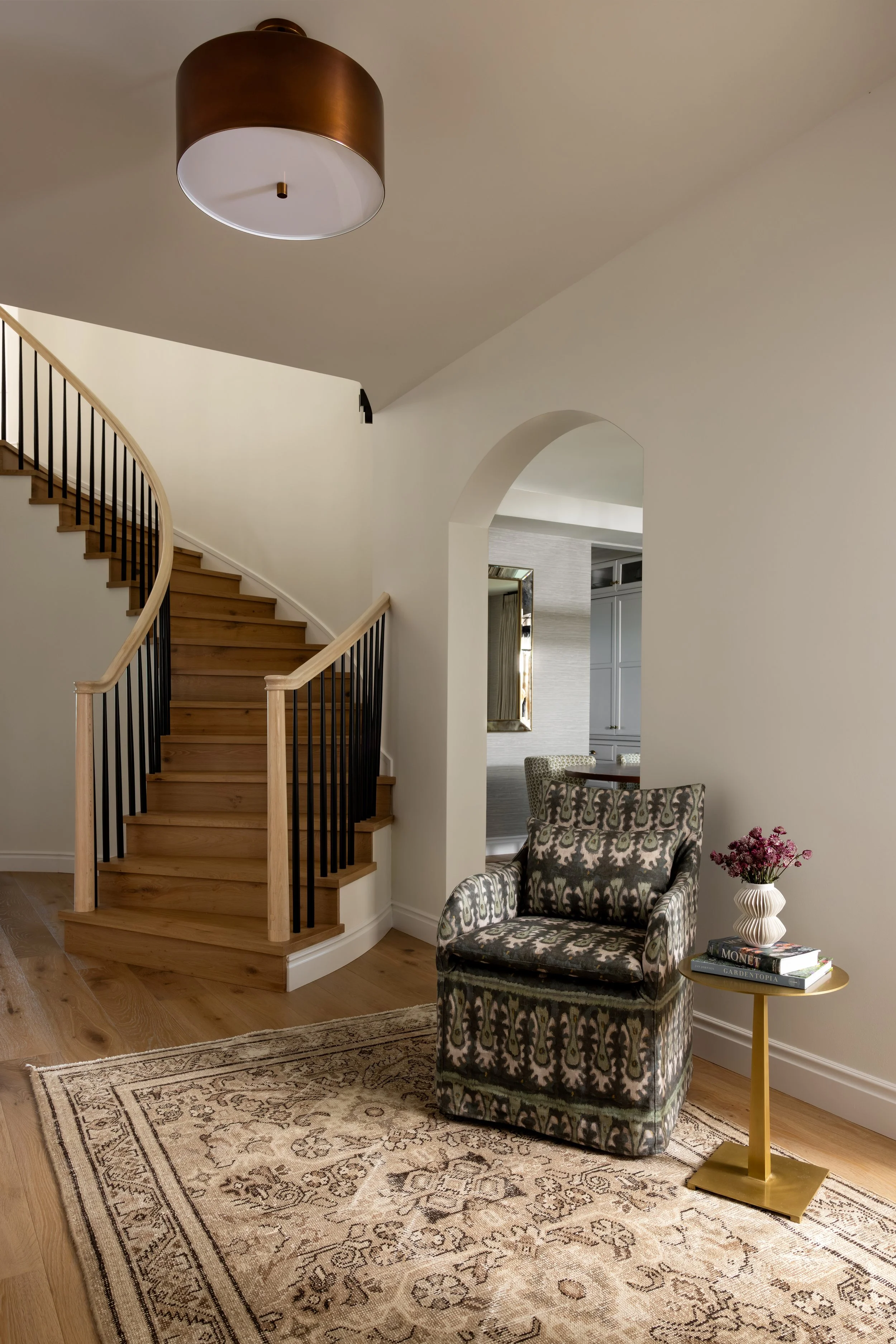 Transitional entryway with curved wood staircase and patterned armchair — Bartlett Residence by Tama Bell Design, Ukiah CA