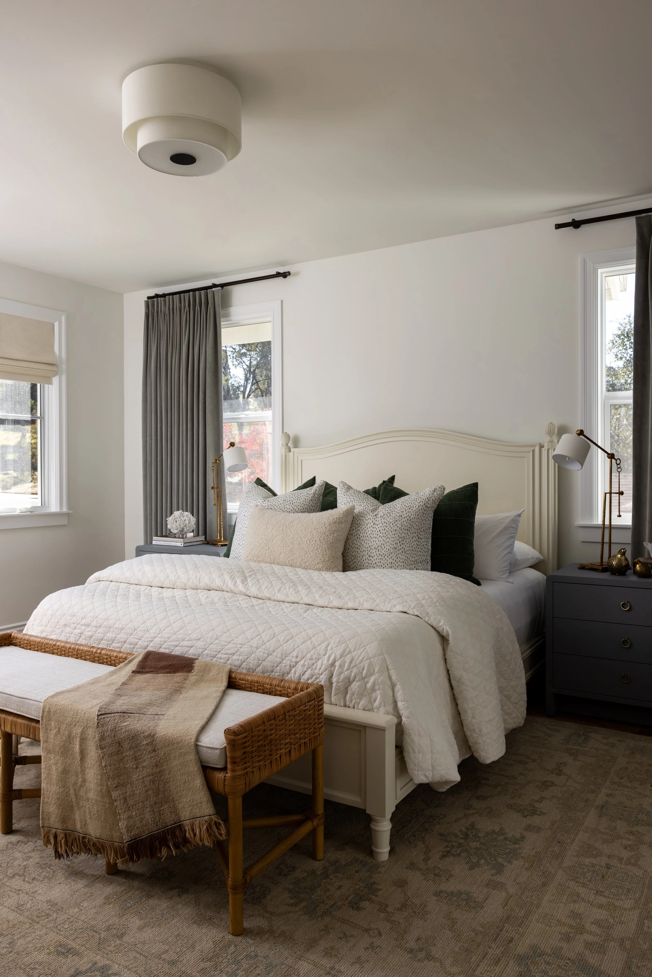 Guest bedroom wide view with cream headboard, quilted bedding, green velvet pillows, gray curtains, and rattan bench — Bartlett Residence by Tama Bell Design, Ukiah CA