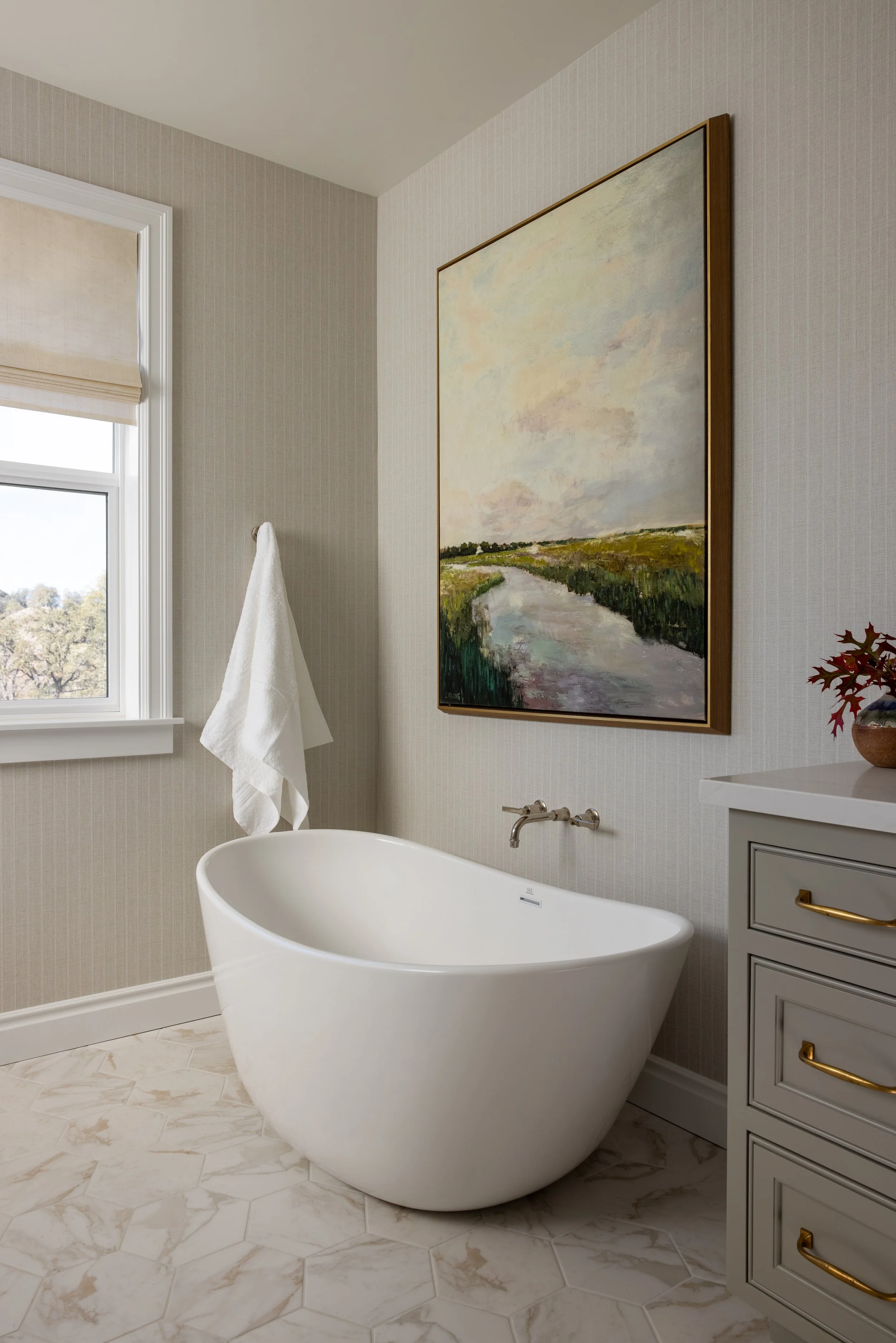 Primary bathroom freestanding soaking tub with wall-mount faucet, landscape painting, and mosaic tile floor — Bartlett Residence by Tama Bell Design, Ukiah CA