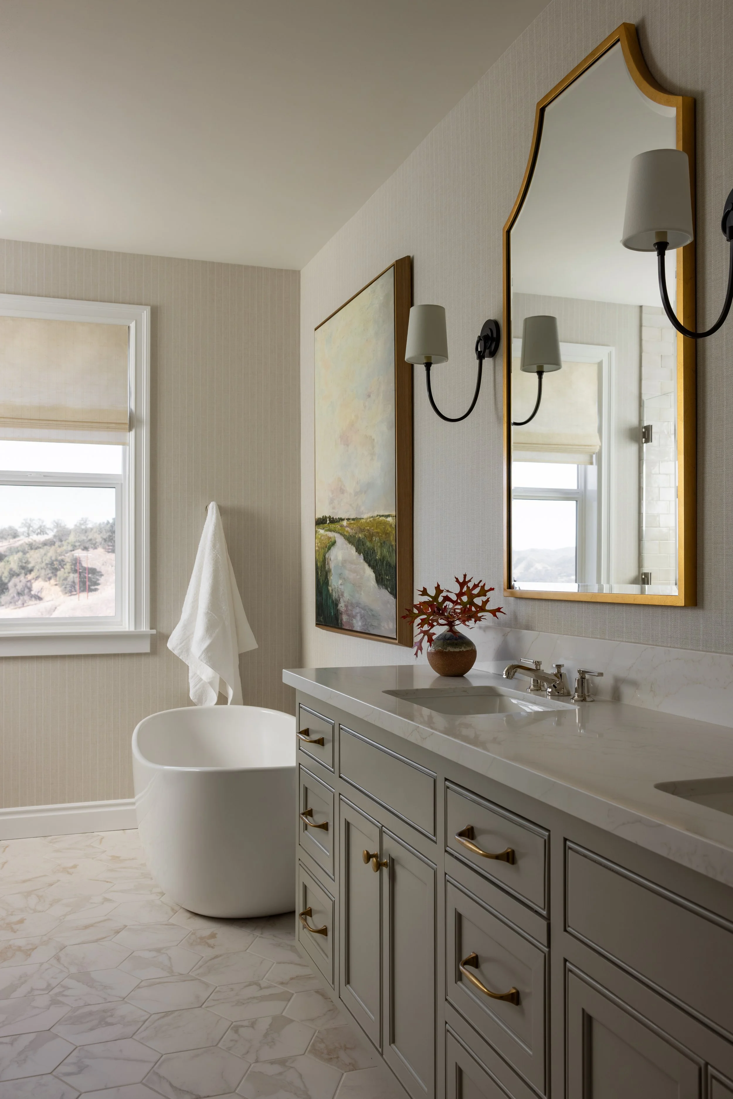 Primary ensuite bathroom with gray vanity, gold framed mirror, freestanding soaking tub, and landscape artwork — Bartlett Residence by Tama Bell Design, Ukiah CA