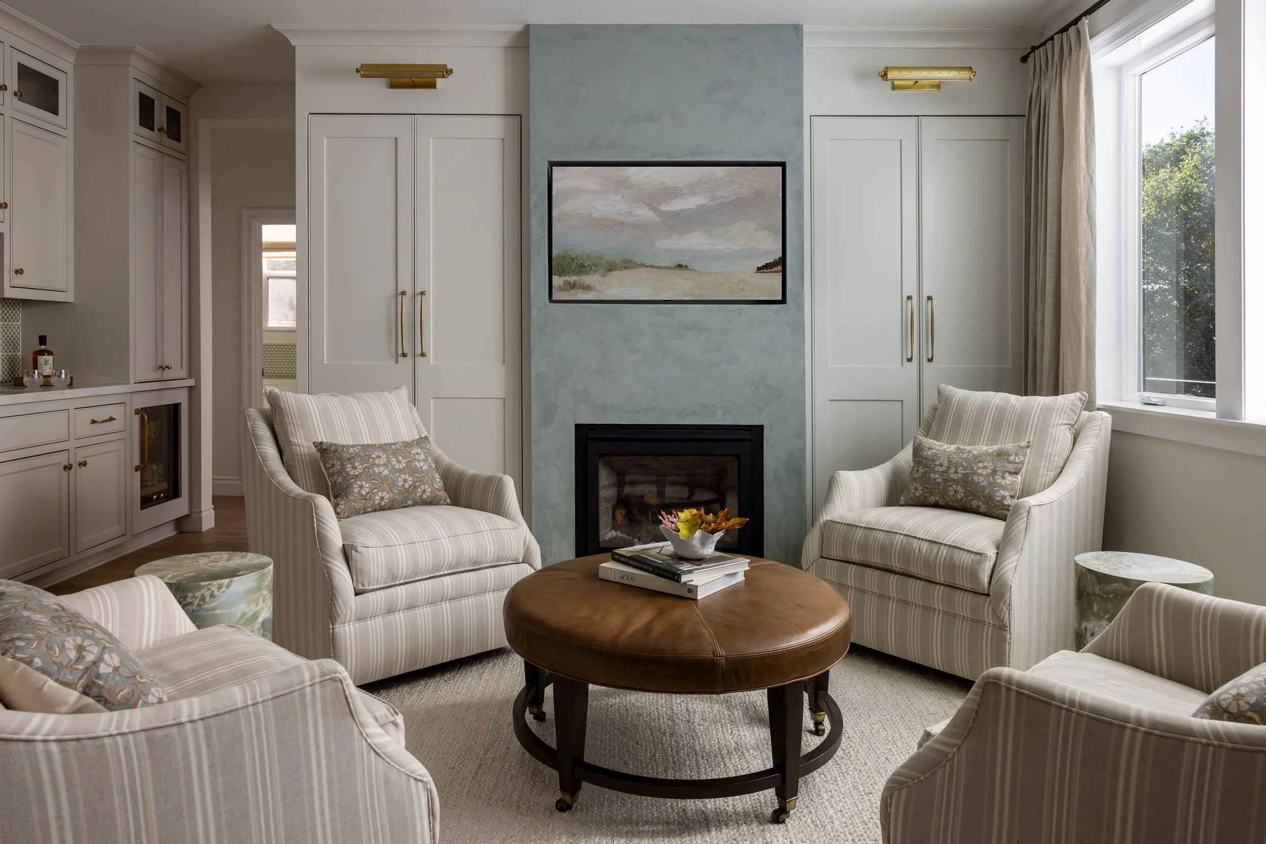 Transitional sitting room with blue plaster fireplace, striped armchairs, leather ottoman, and built-in cabinetry — Bartlett Residence by Tama Bell Design, Ukiah CA