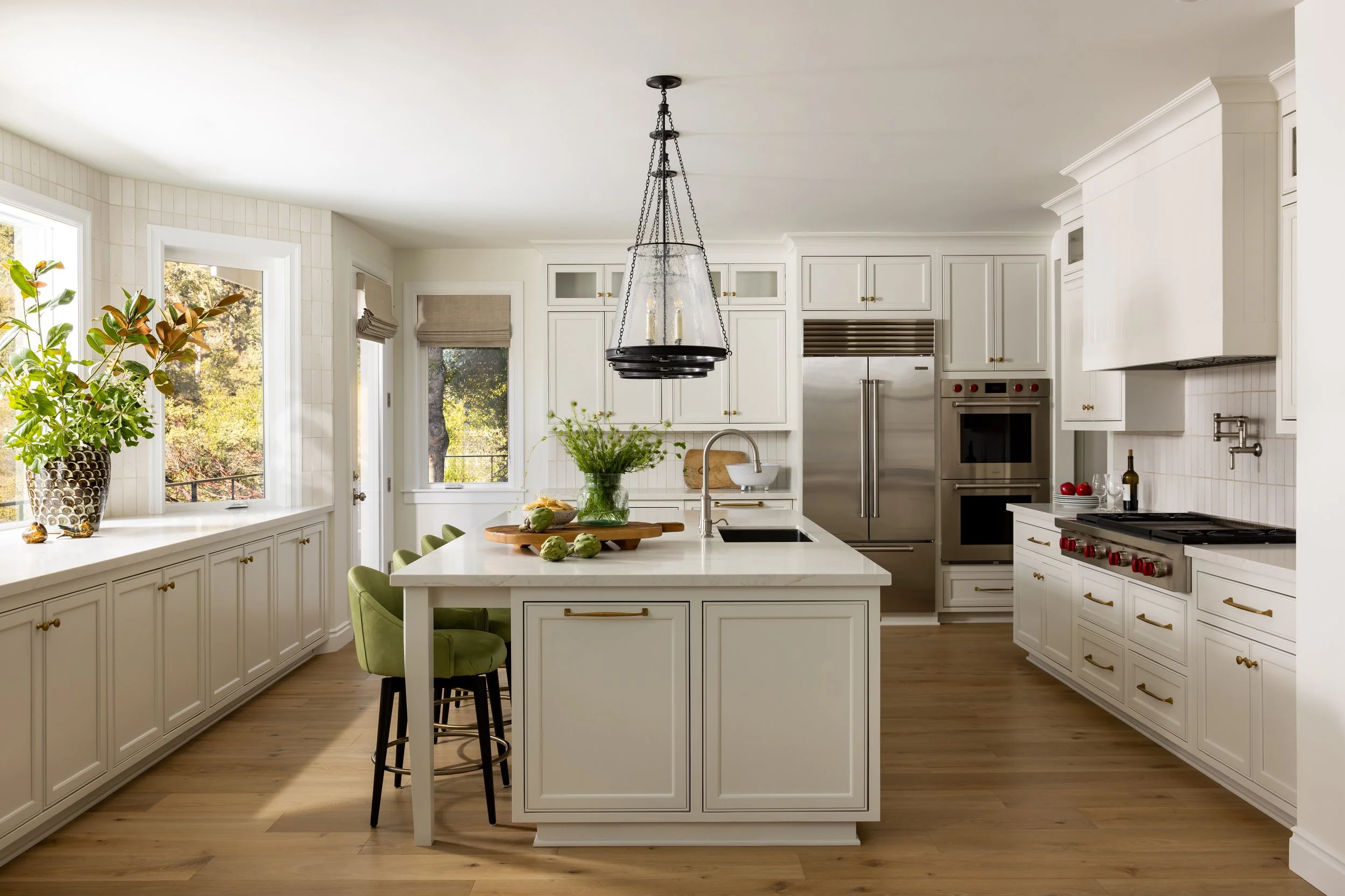 Transitional white kitchen with center island, green velvet barstools, brass hardware, and black pendant light — Bartlett Residence by Tama Bell Design, Ukiah CA
