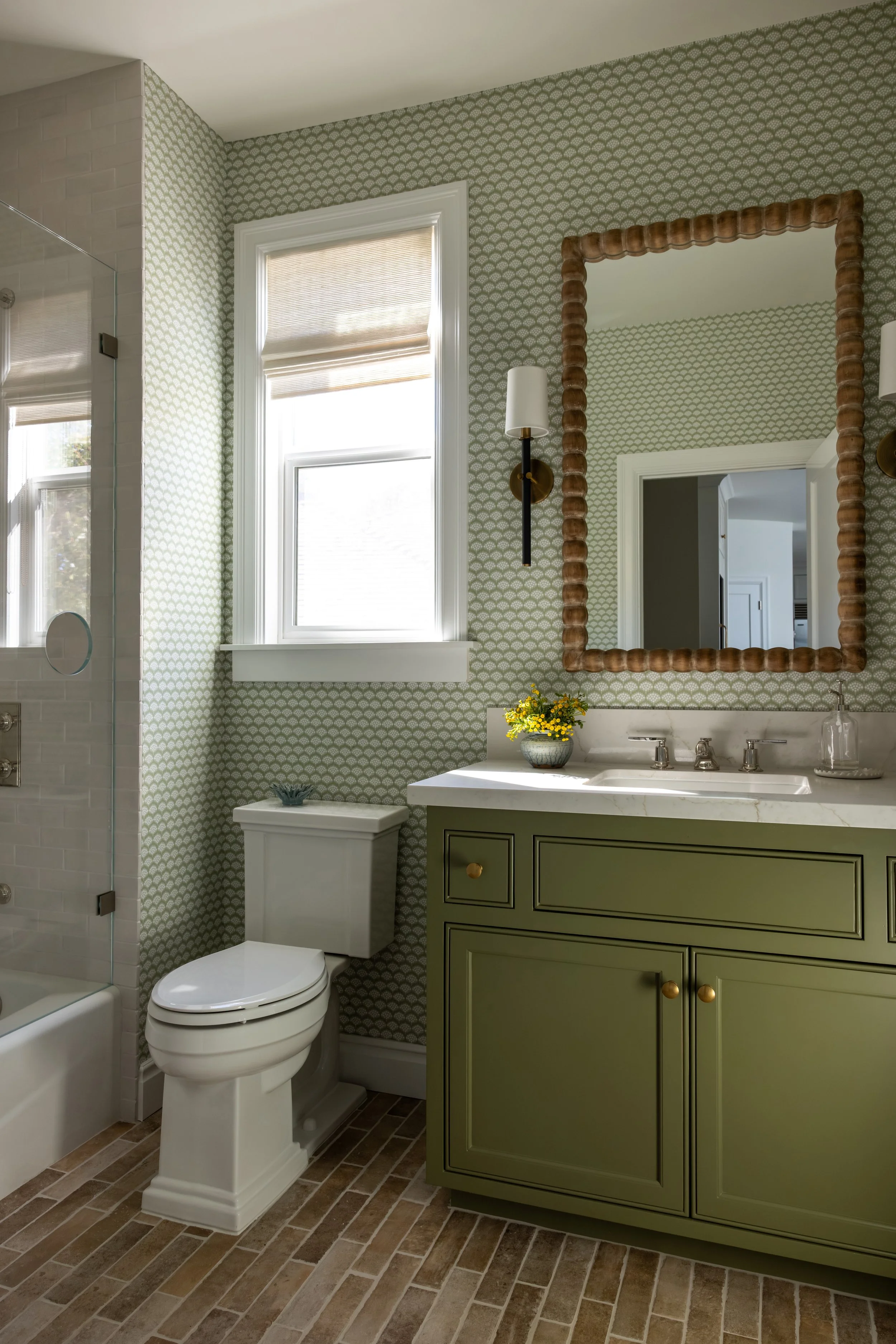 Transitional bathroom with olive green vanity, scallop wallpaper, rattan mirror, and brick tile floor — Bartlett Residence by Tama Bell Design, Ukiah CA