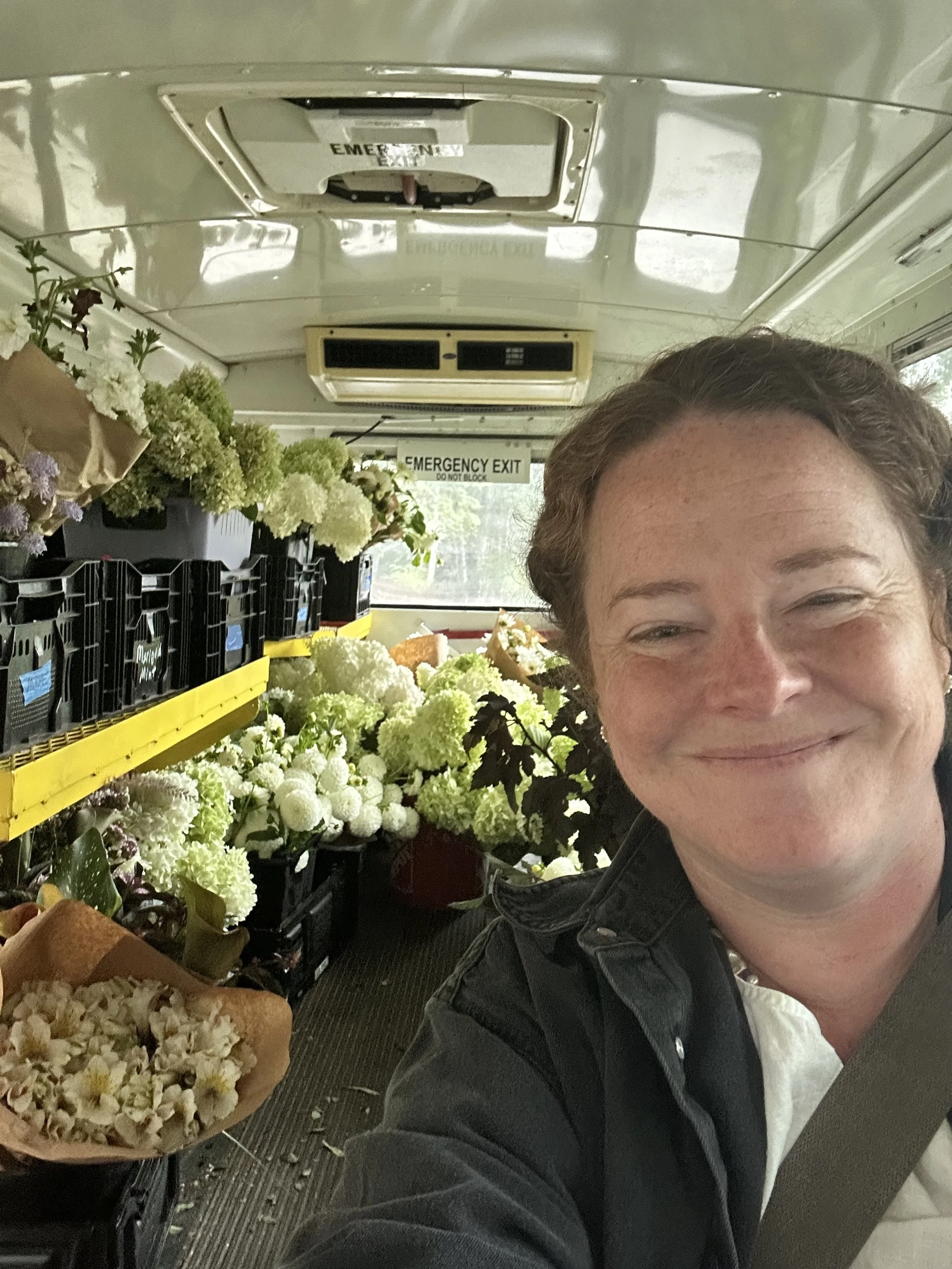 A smiling delivery driver in The Flower Bus full of locally grown flowers.