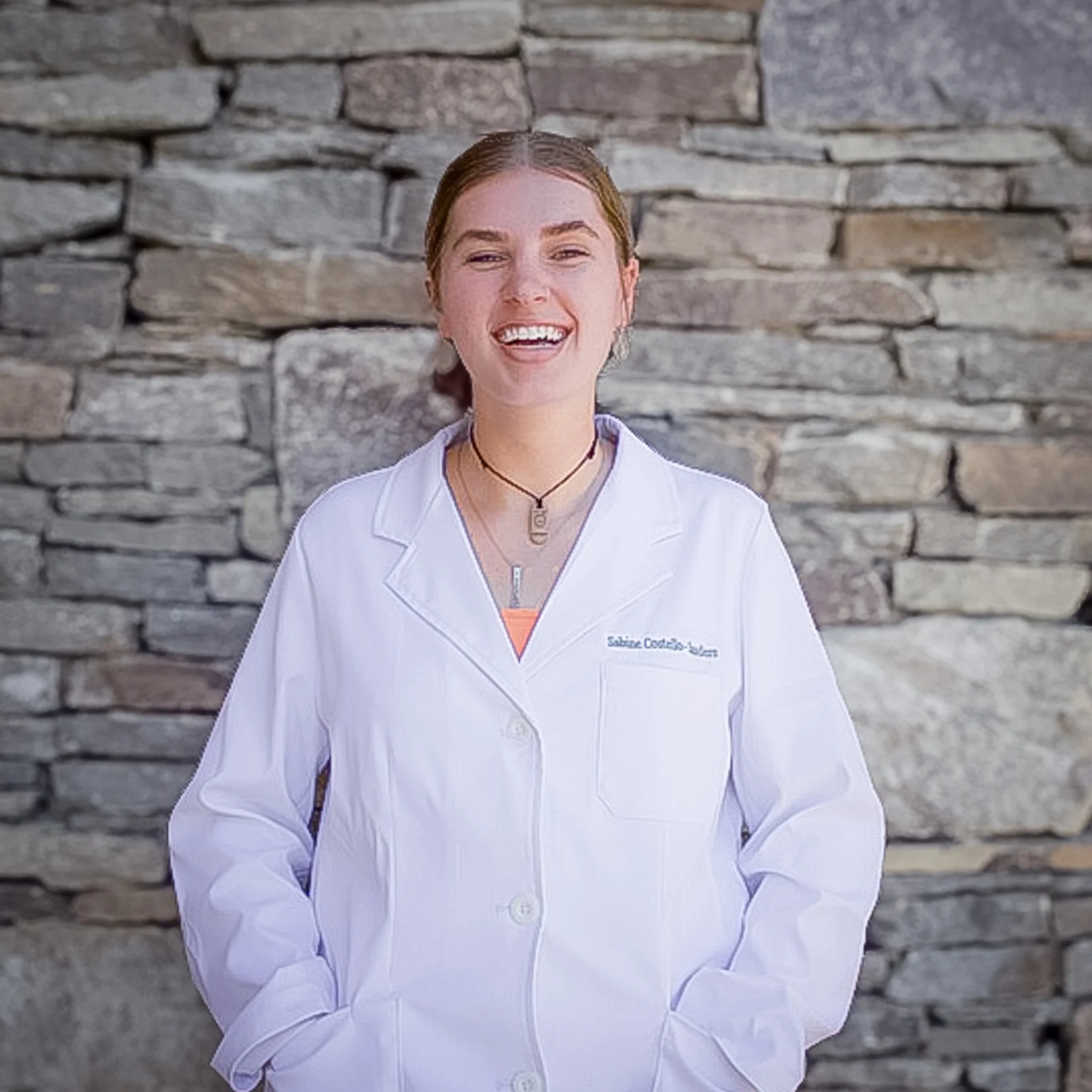 A young lady smiling in a lab coat, with a stone backdrop