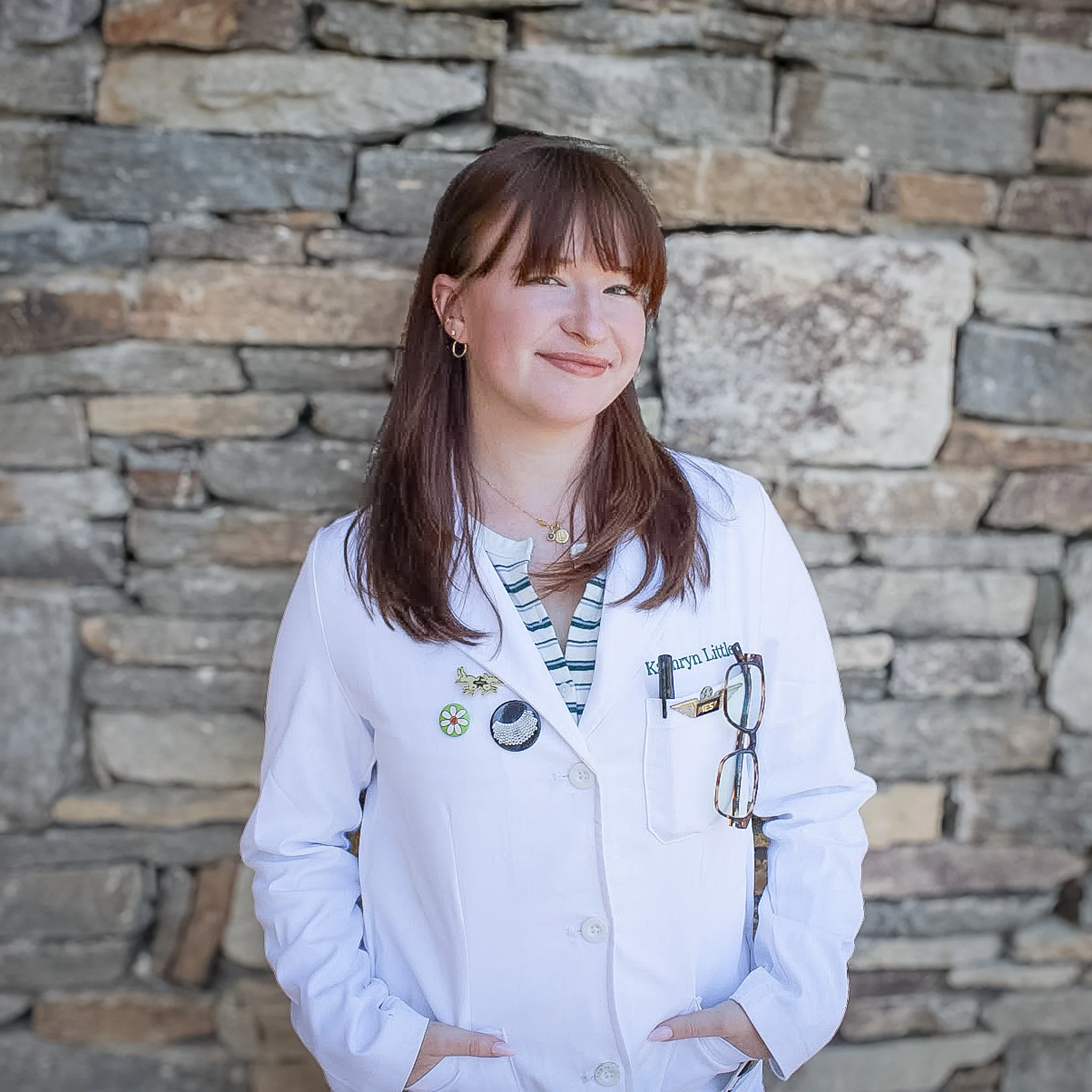 A young lady smiling in a lab coat, with a stone backdrop