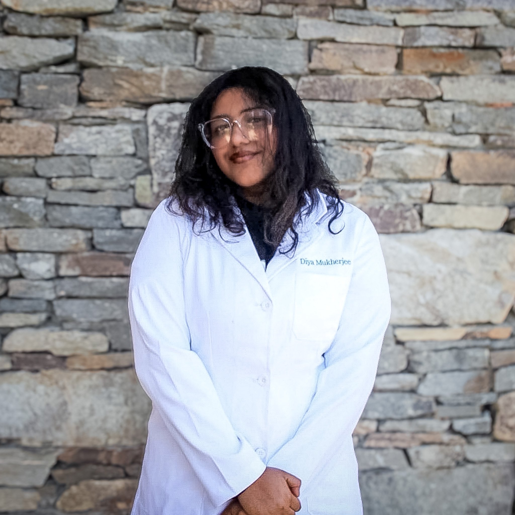 A young lady smiling in a lab coat, with a stone backdrop