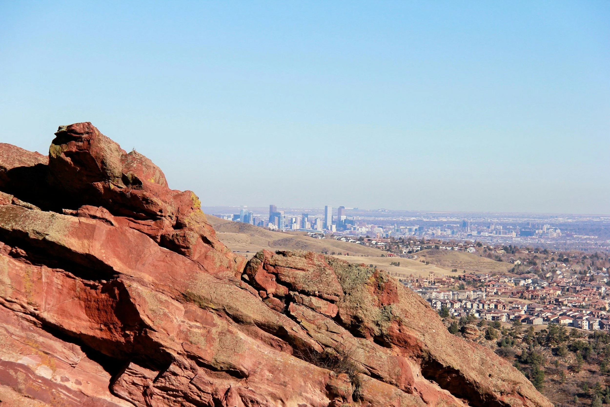 Red rock formation with a distant view of a city skyline in the background.