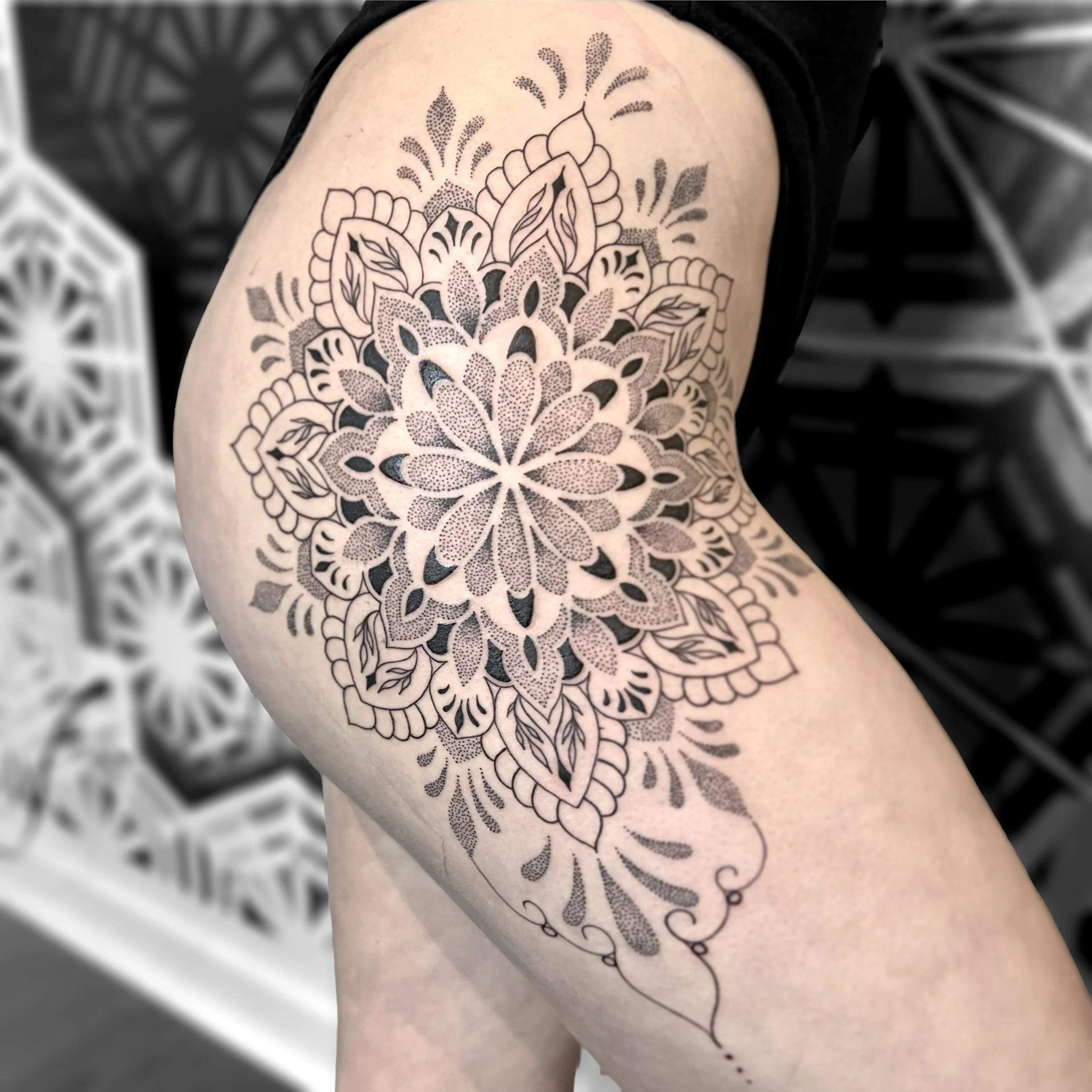 A black ink floral mandala tattoo on a person's thigh, featuring detailed petal and leaf patterns with shading and dot work.