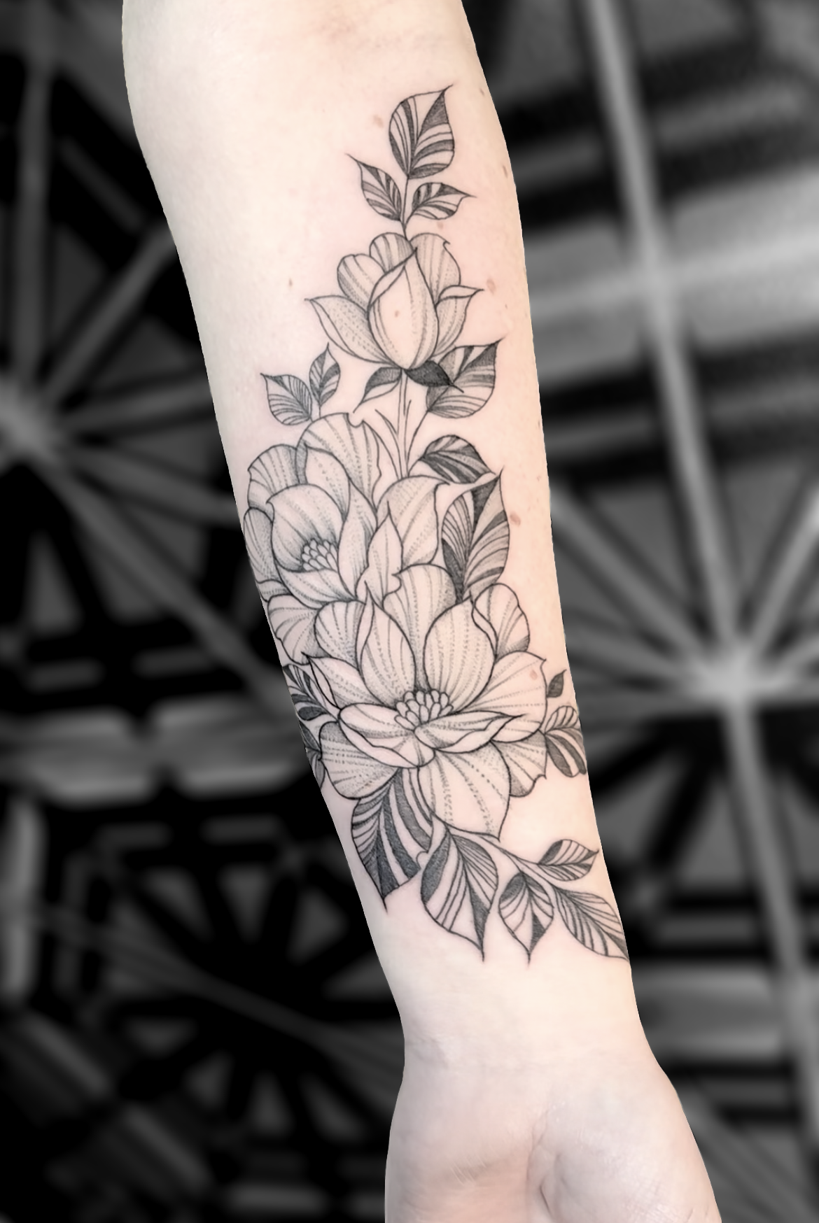 Black and gray floral tattoo on inner forearm, featuring detailed flowers and leaves.