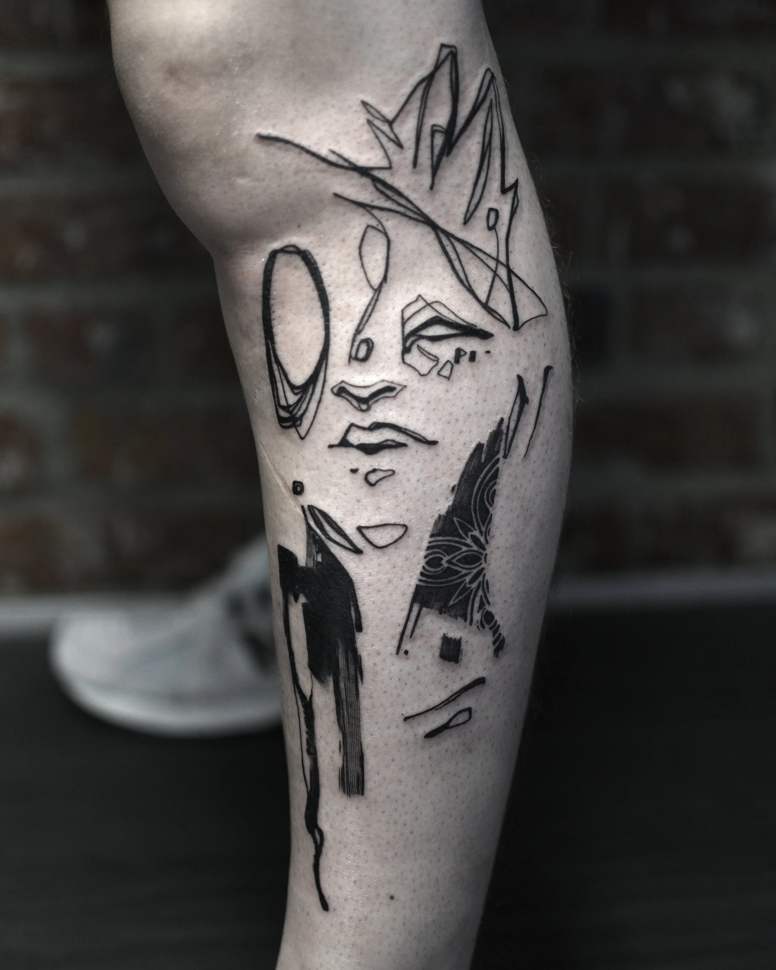 Abstract black line tattoo on leg with geometric and artistic elements.