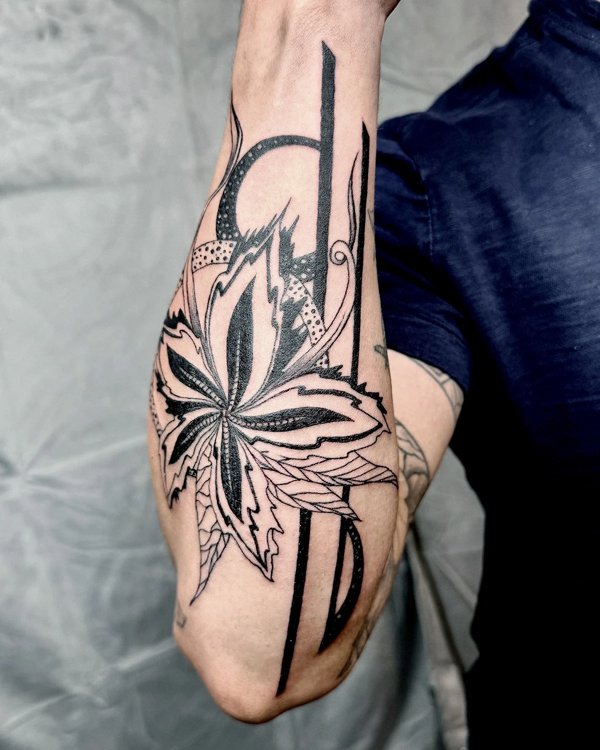 Black and gray tattoo of a large flower with detailed leaves on a person's forearm.