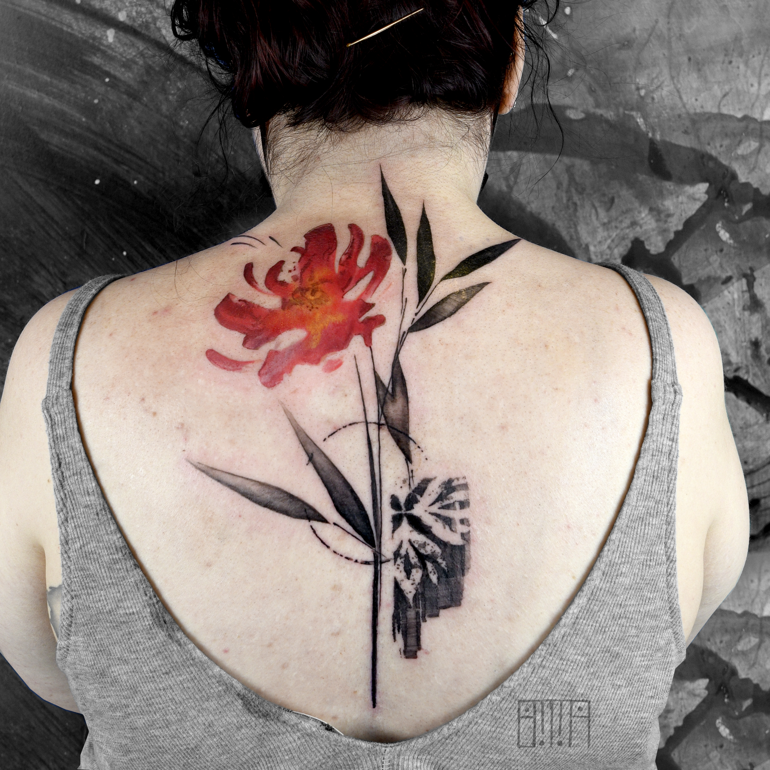 A woman with a shoulder tattoo of a red flower and green leaves on her upper back, wearing a gray tank top.