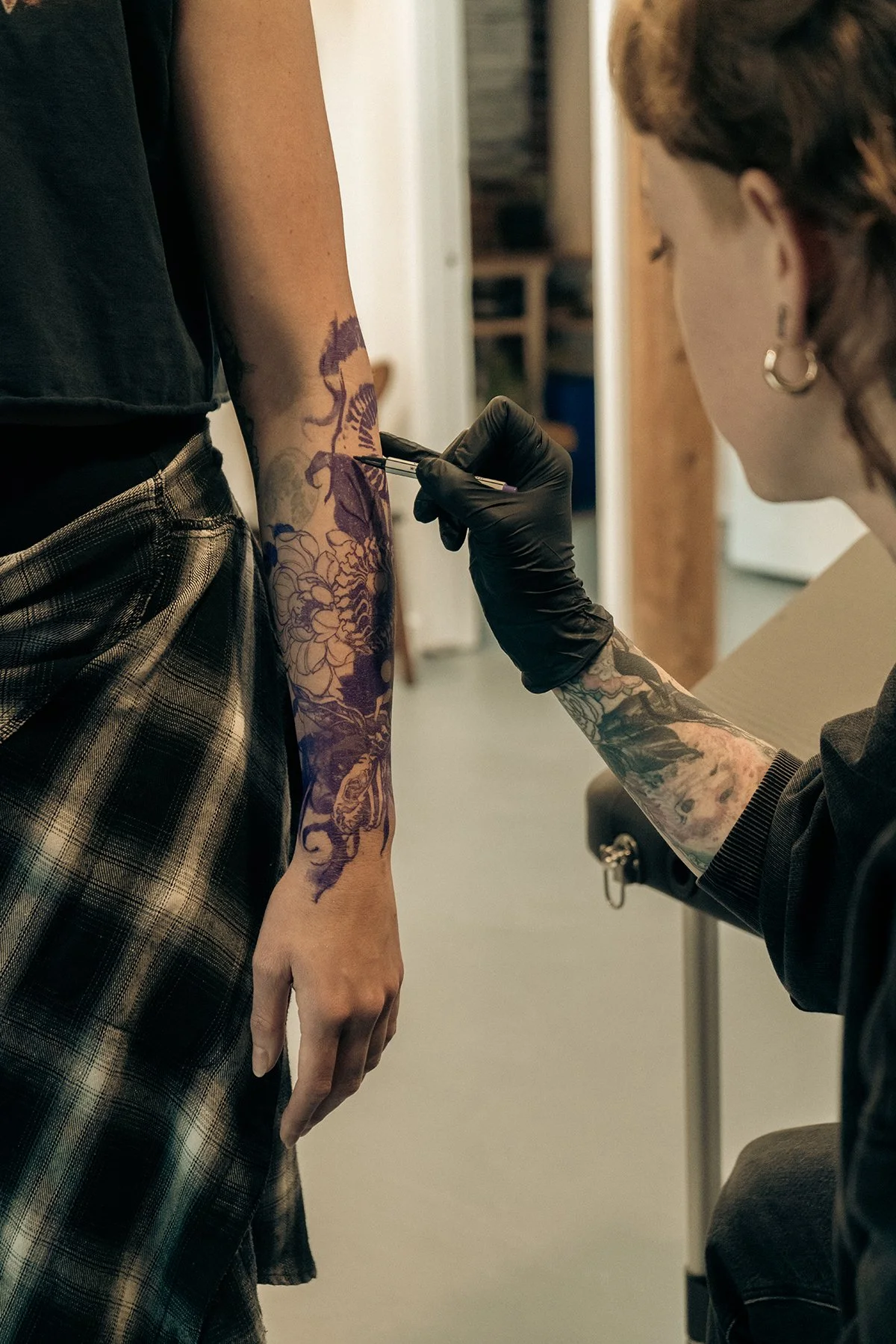 Tattoo artist drawing a design on a person's forearm with a stencil in a studio.