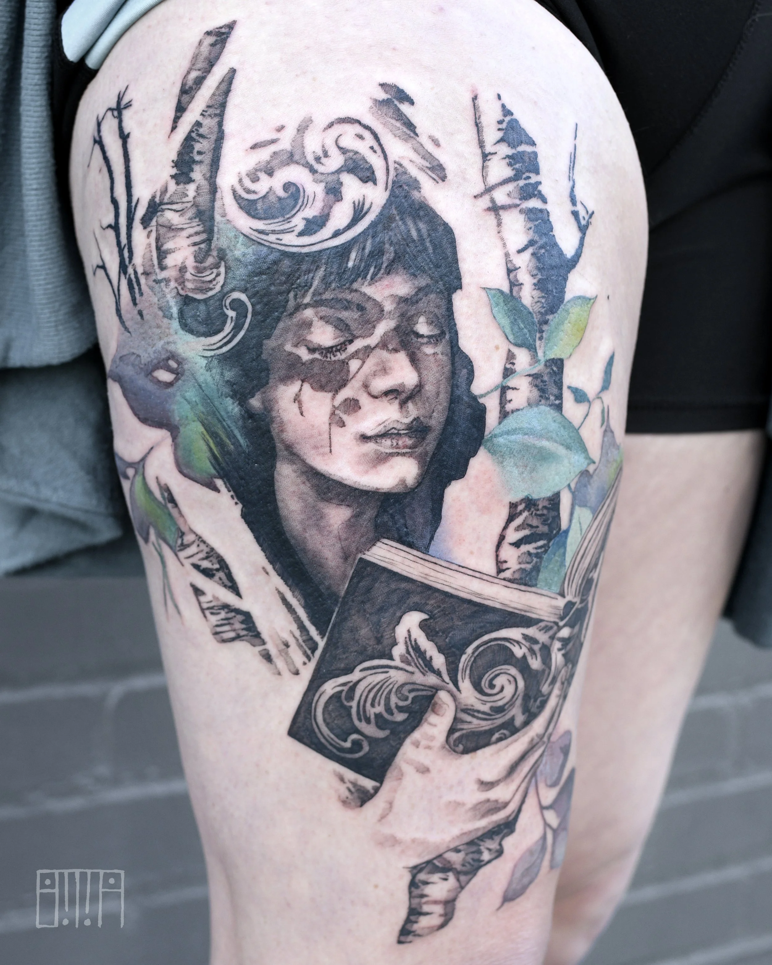 Tattoo of a woman's face with closed eyes, surrounded by trees and decorative elements, on a person's upper arm.