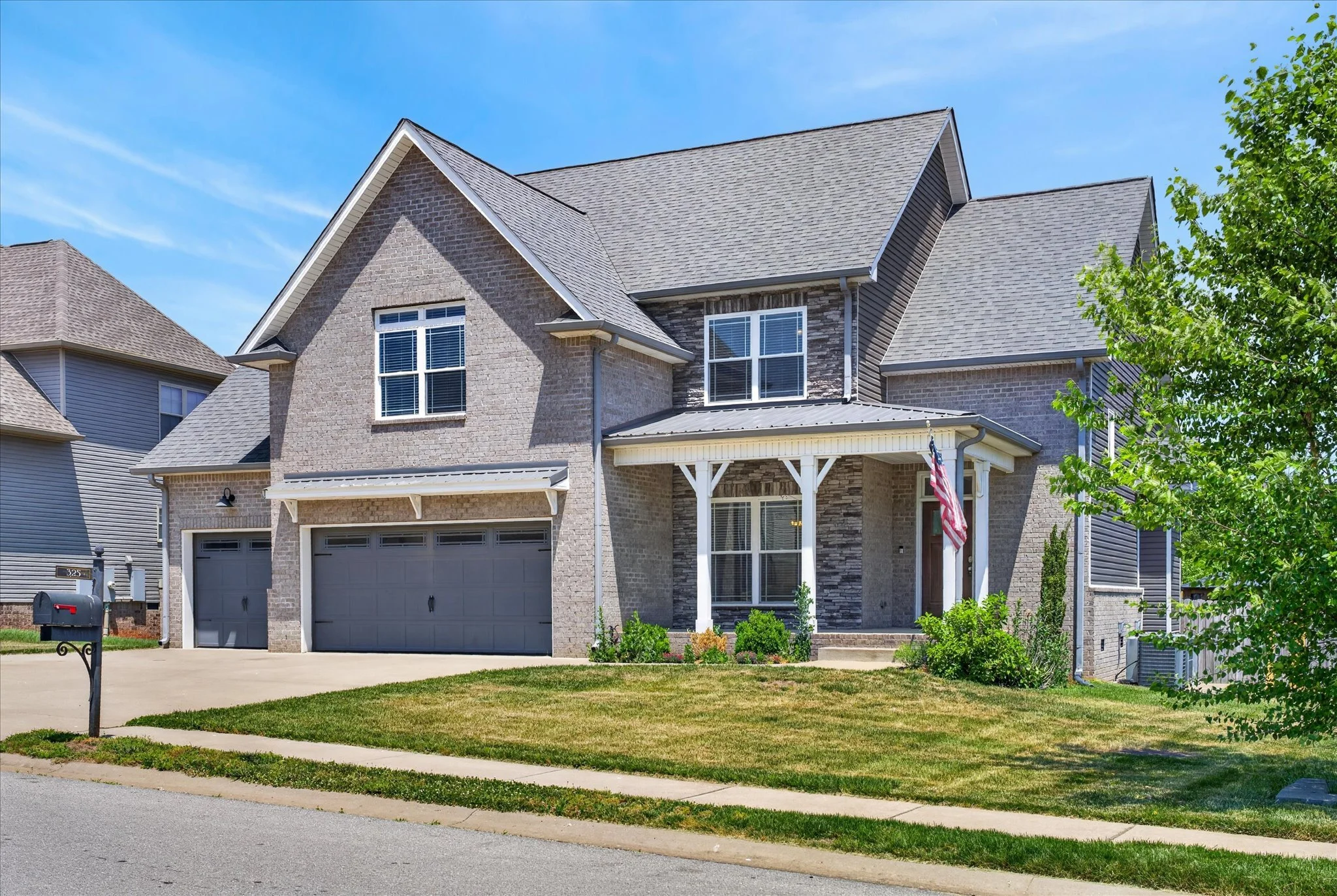 White two-story house with brown front door, green lawn, and neighboring homes on a sunny day with blue sky