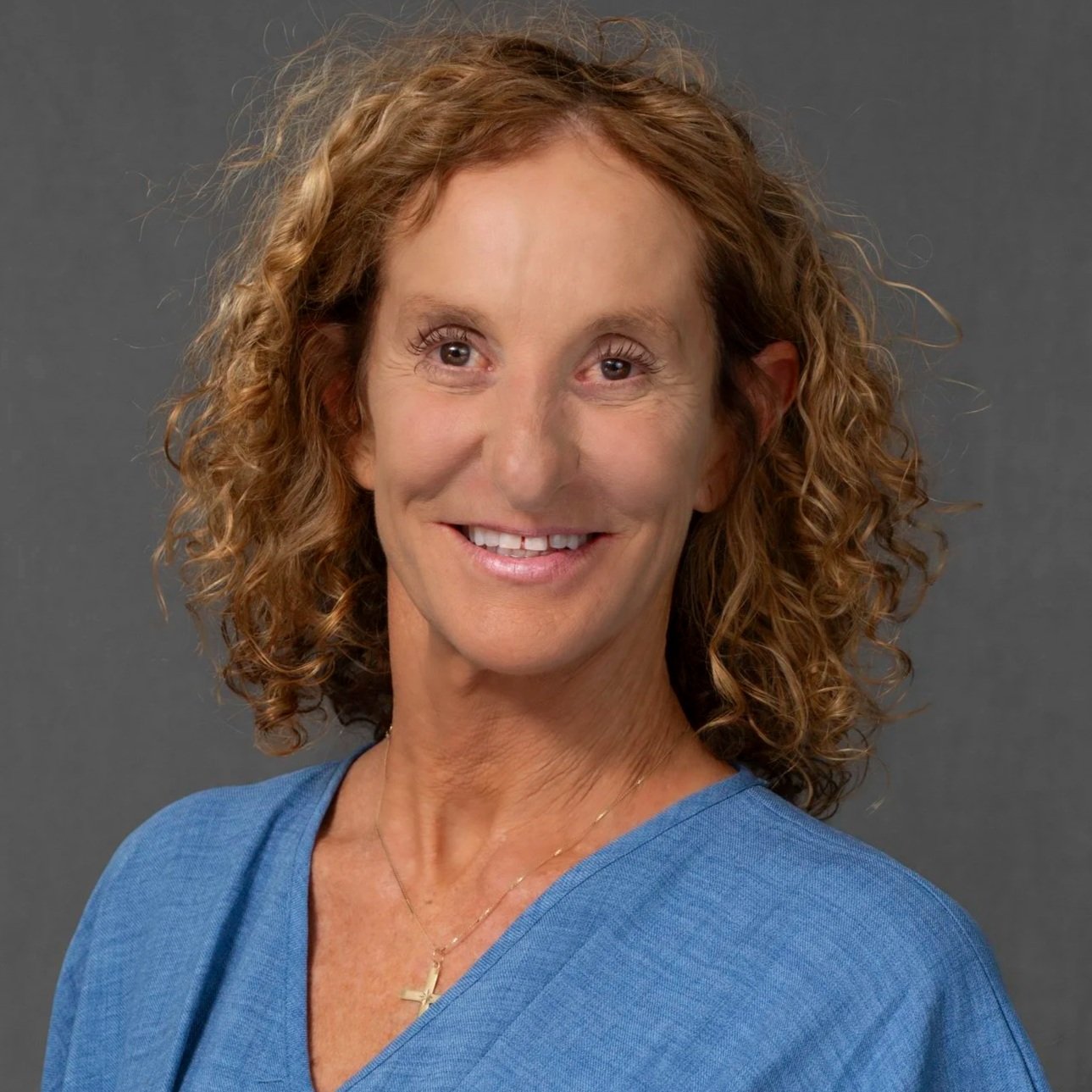 Woman with curly red hair wearing a black turtleneck, smiling in front of a dark background.