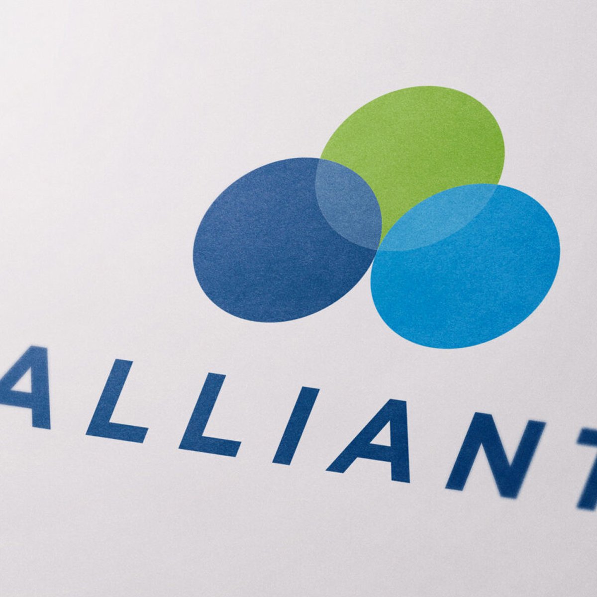 Close-up of a logo with four overlapping circles in blue and green above the partial word 'ALLIANCE' in blue uppercase letters on a white background.
