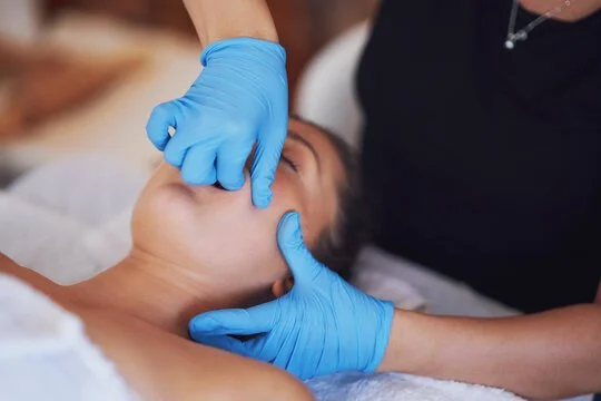 A healthcare professional wearing blue gloves examining a woman's throat or mouth during a medical check-up.