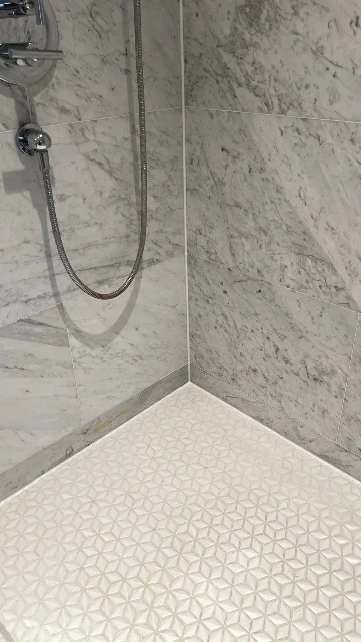 Newly restored tile and grout in and repaired shower showing shower wall, floor and hose