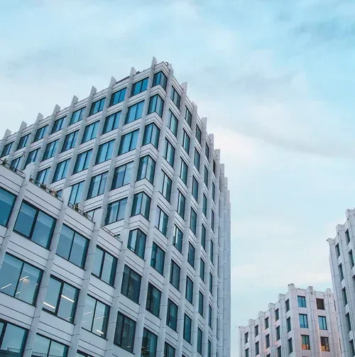 Un immeuble moderne avec de nombreuses fenêtres en verre, vue partielle contre un ciel bleu avec quelques nuages.