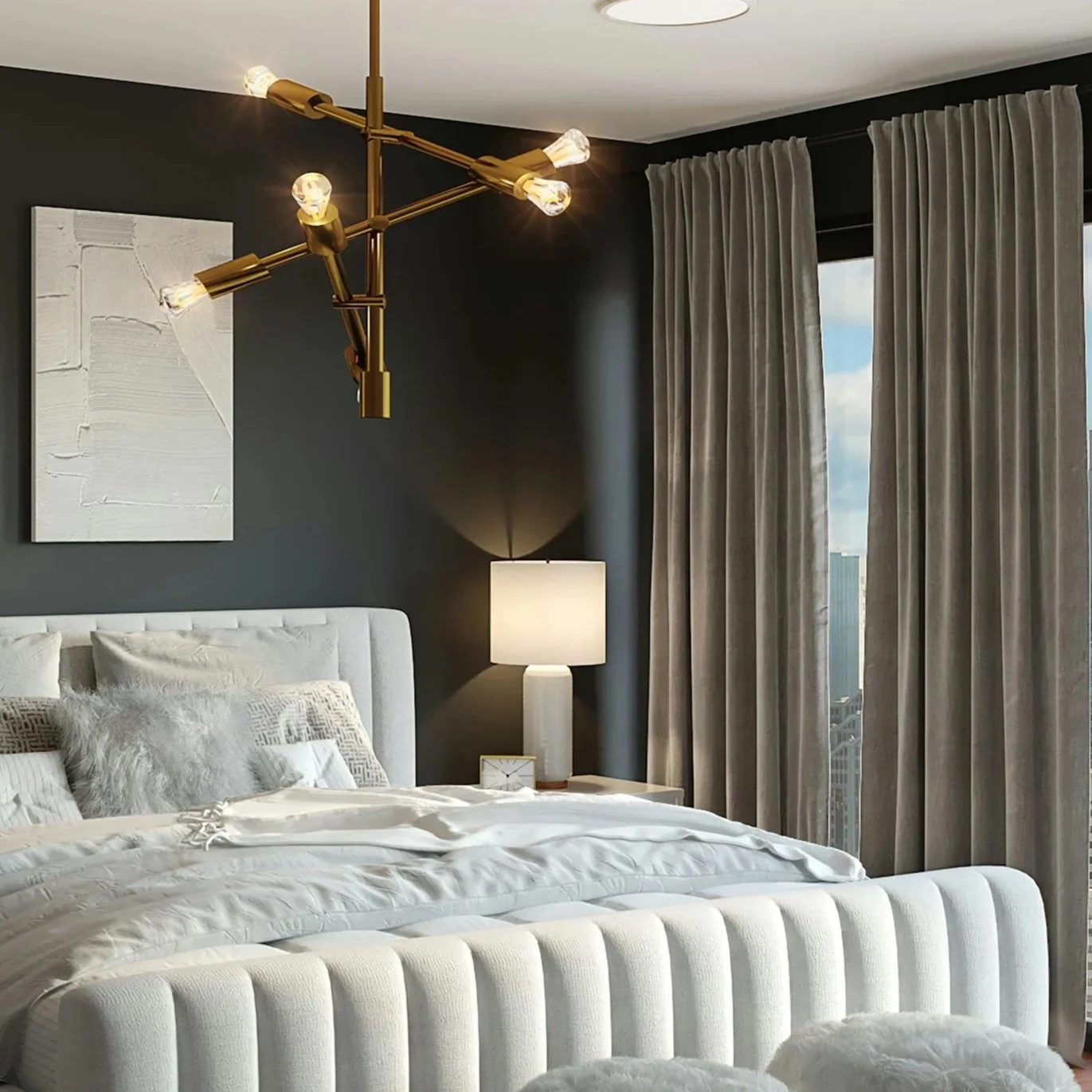 A modern bedroom with a white upholstered bed, grey and beige pillows, a white bedside table with a white table lamp, a dark accent wall with a piece of abstract art, and a large window with grey curtains showing city buildings outside.