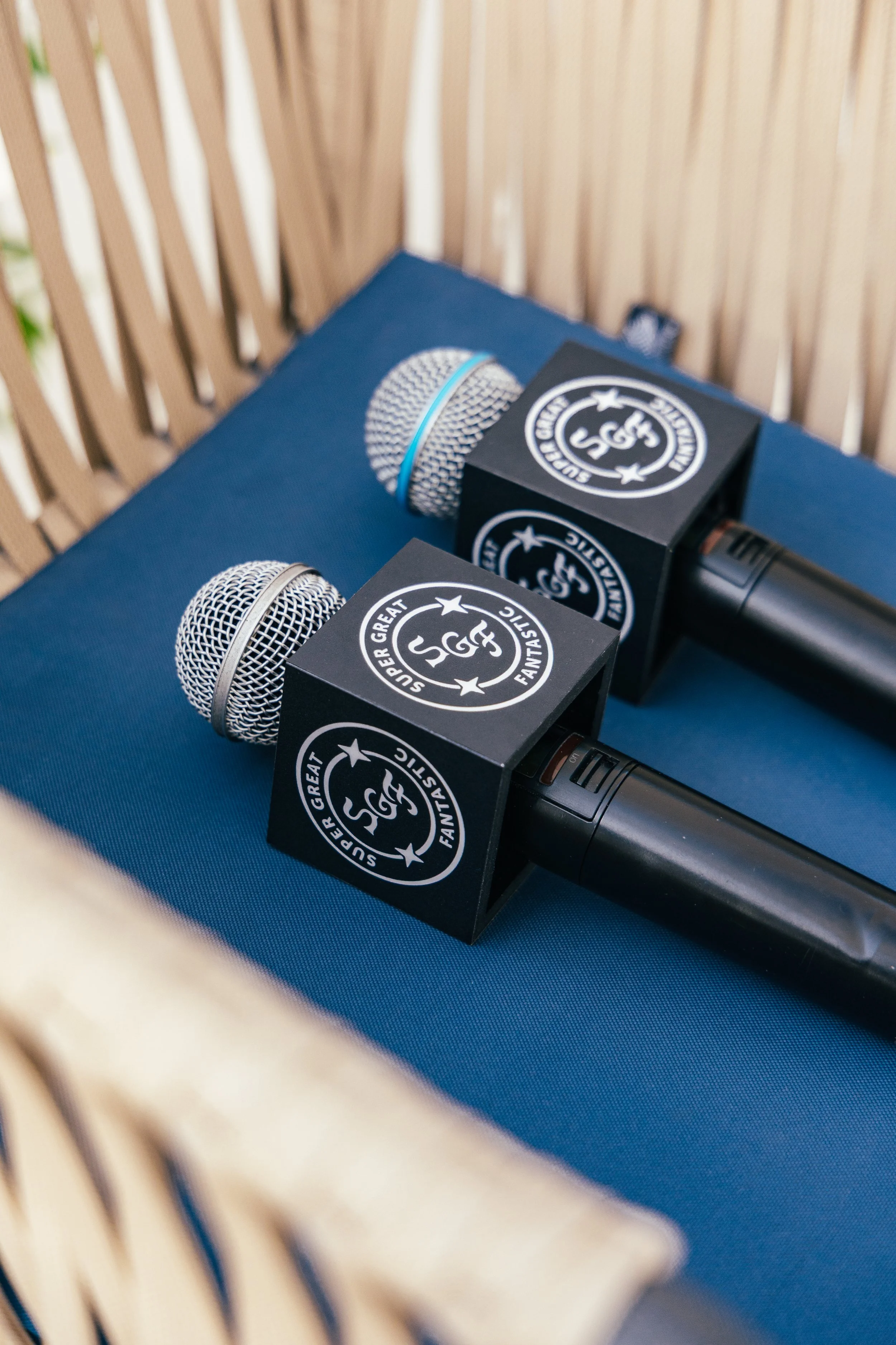 Two microphones with black foam covers and branded boxes resting on a blue surface, with a wooden slat background.