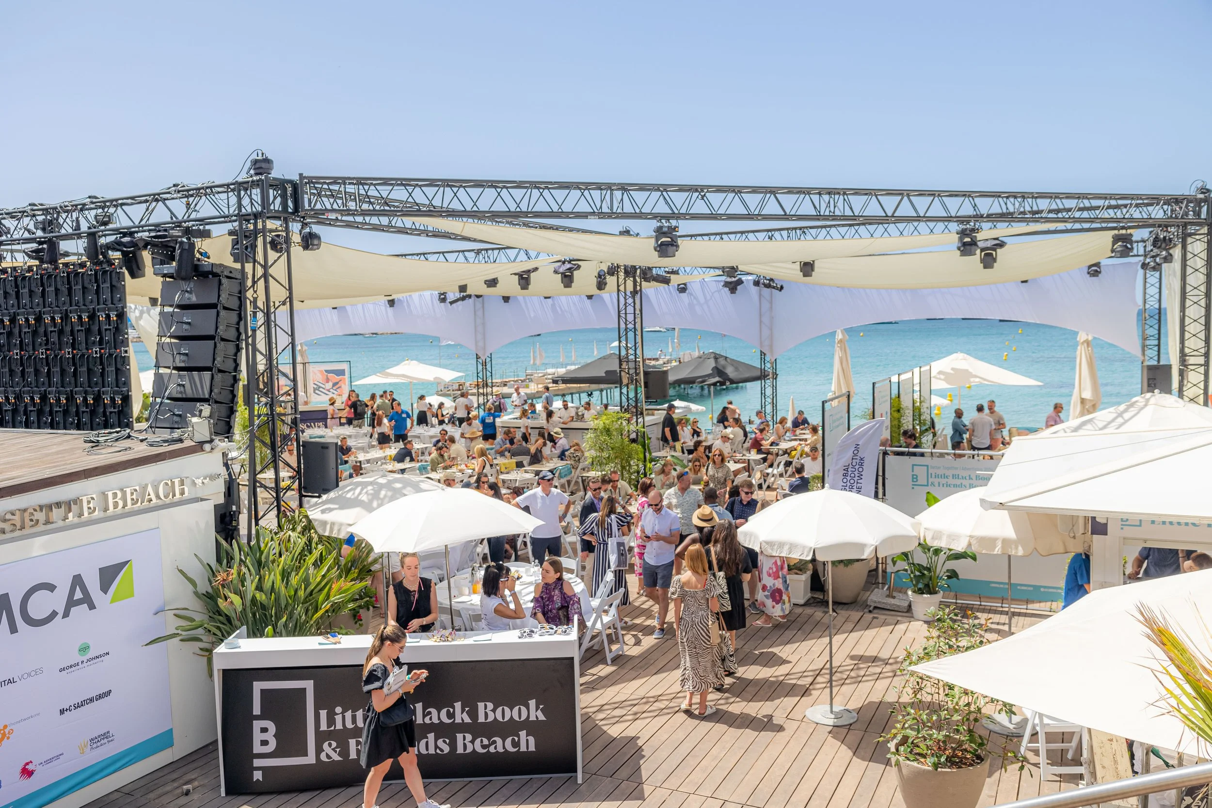 Beachside event at Little Black Book & Friends Beach with people sitting under umbrellas and enjoying the sunny day by the ocean