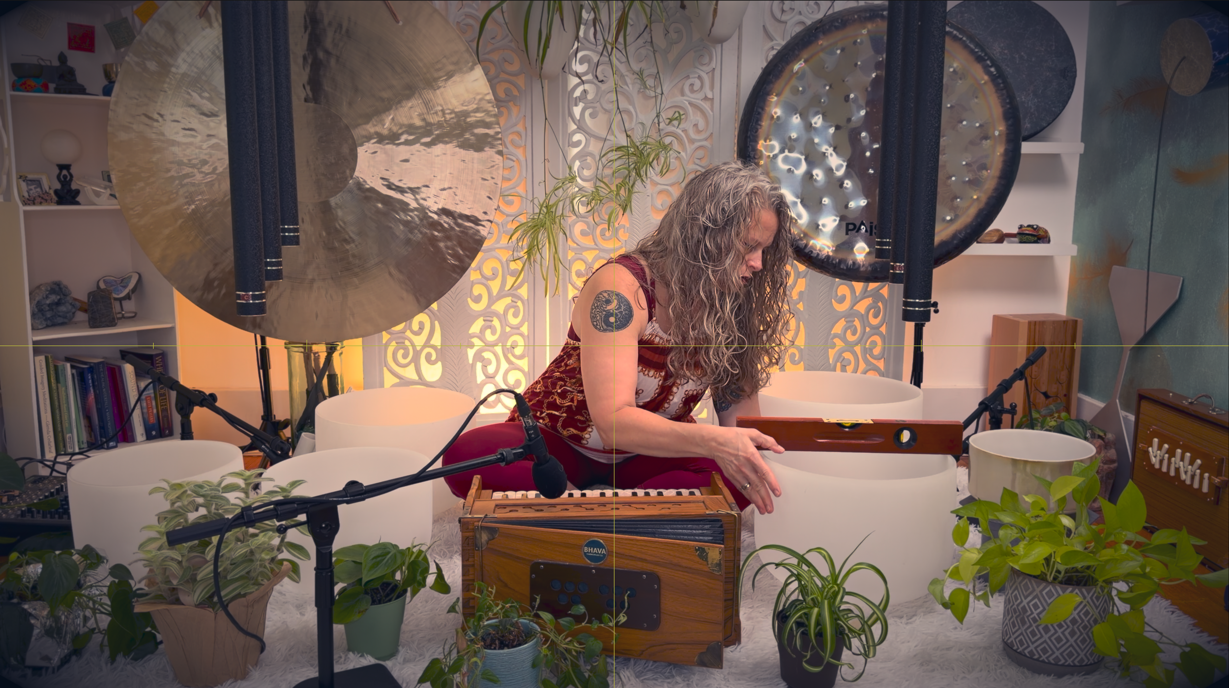 Photograph of a woman sitting cross-legged surrounded by crystal bowls with a level on one of the bowls.