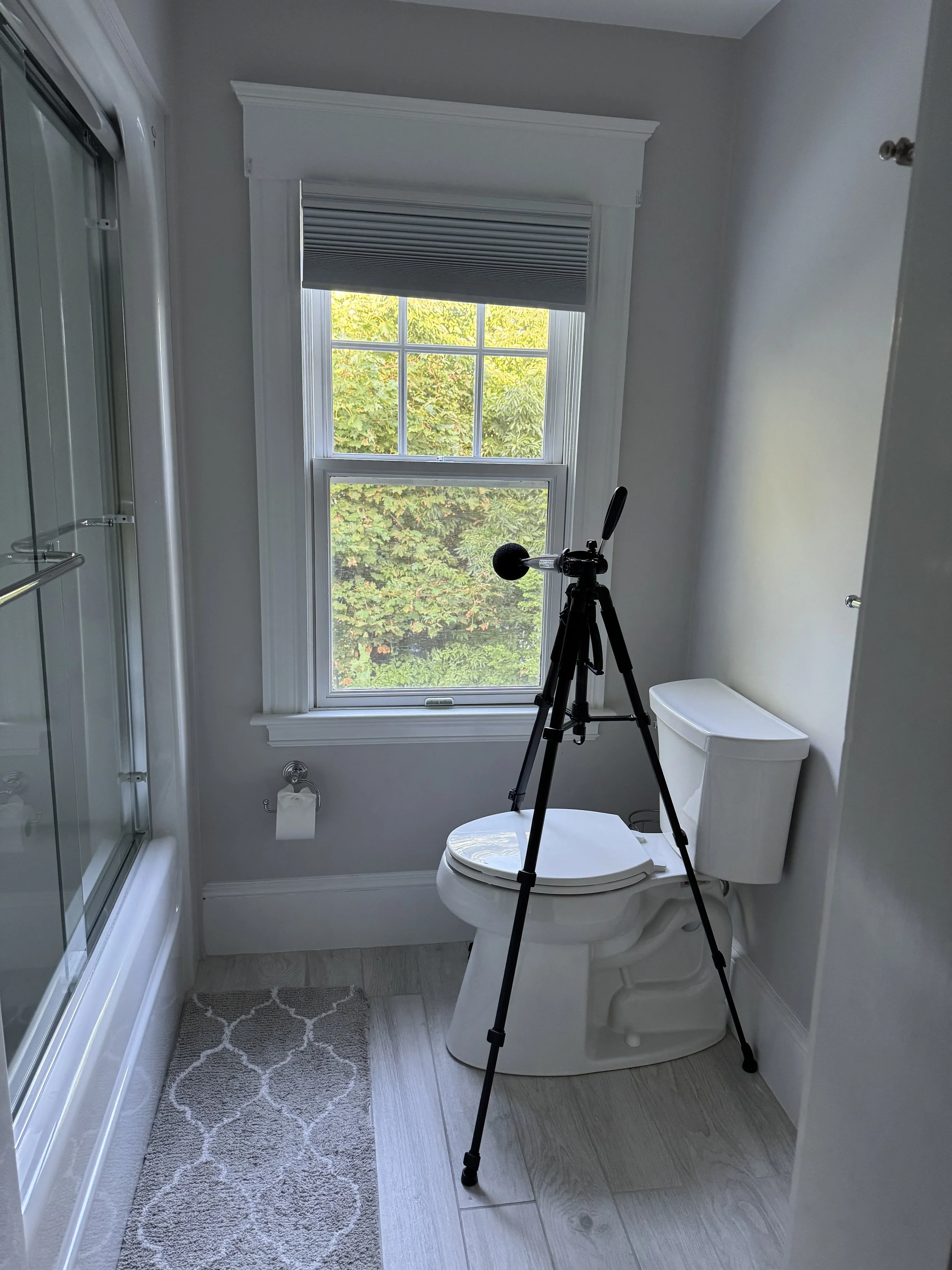 Noise impact. Bathroom with a toilet, a window with a pickleball court nearby, a tripod with a microphone set up in front of the toilet, pickleball noise in every part of your home.  No escape even with windows closed.
