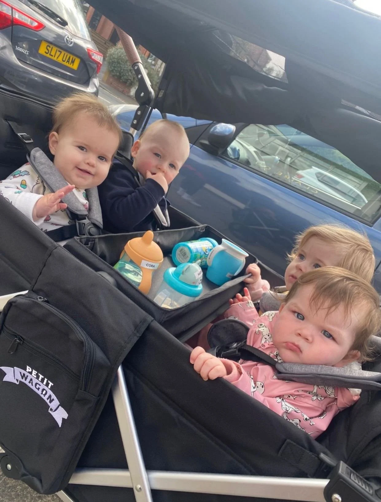 A mother of 3 kids pushing a wagon stroller in the park with comfortable seats and a snack tray